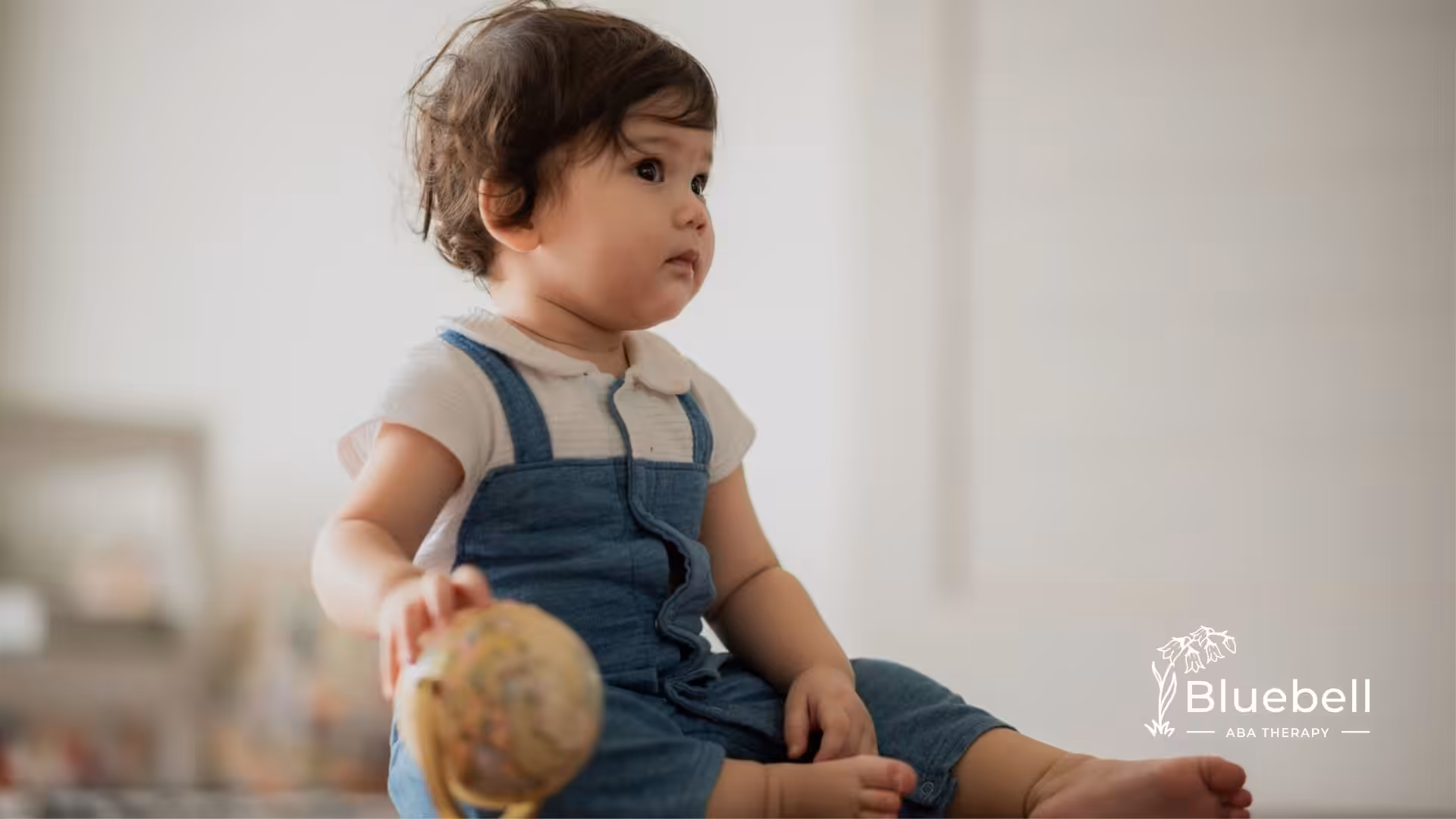 Toddler sitting on the floor holding a small globe during an ABA therapy session.