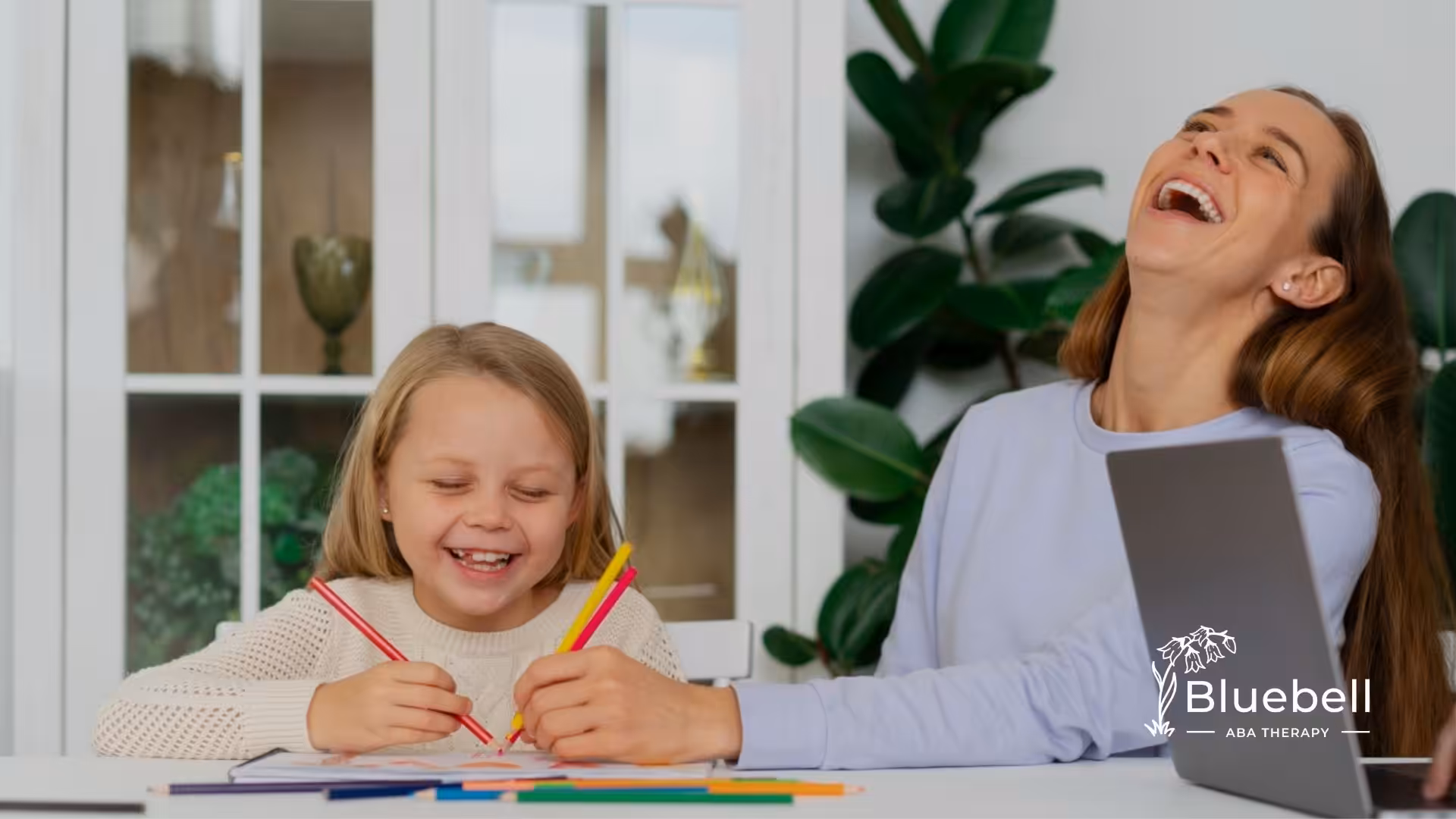 Child and therapist laughing together during an engaging ABA therapy session with art activities.