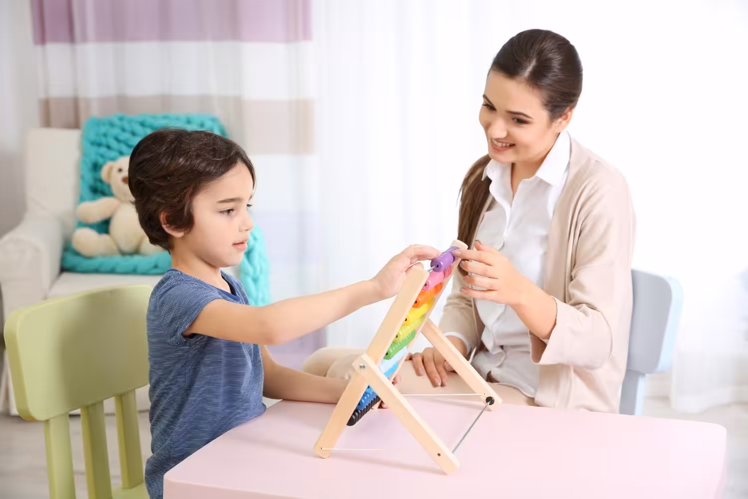 A boy learning to use a rainbow abacus with guidance from an ABA therapist.