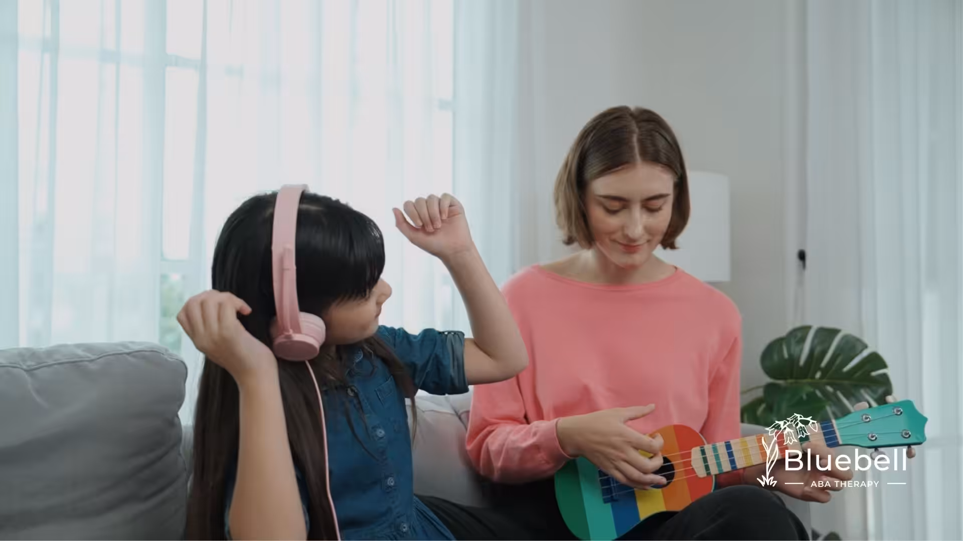A girl wearing headphones dancing while an ABA therapist plays a colorful ukulele.