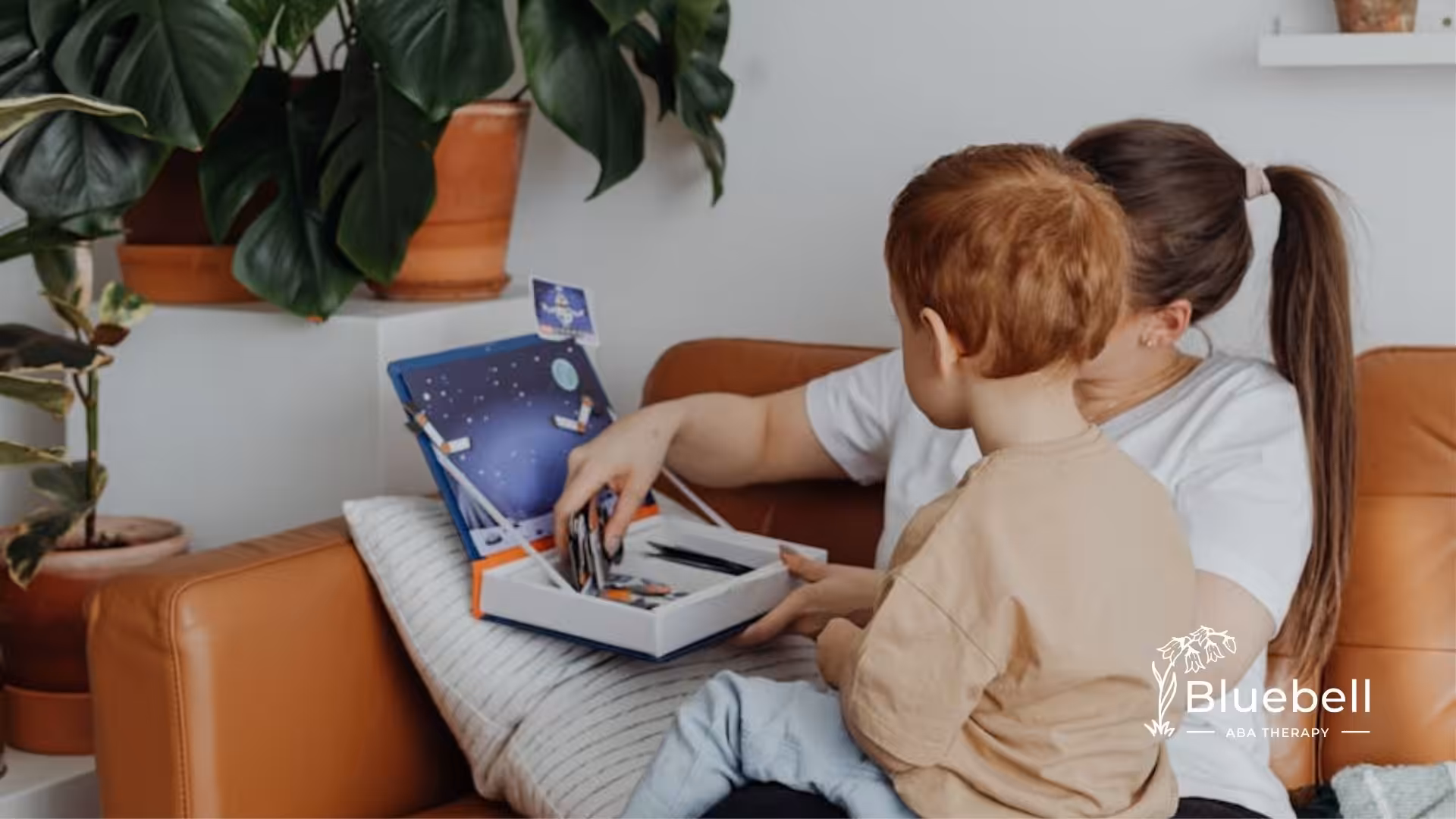 A behavioral therapist and autistic kid sitting on a couch looking through an activity book in NC.