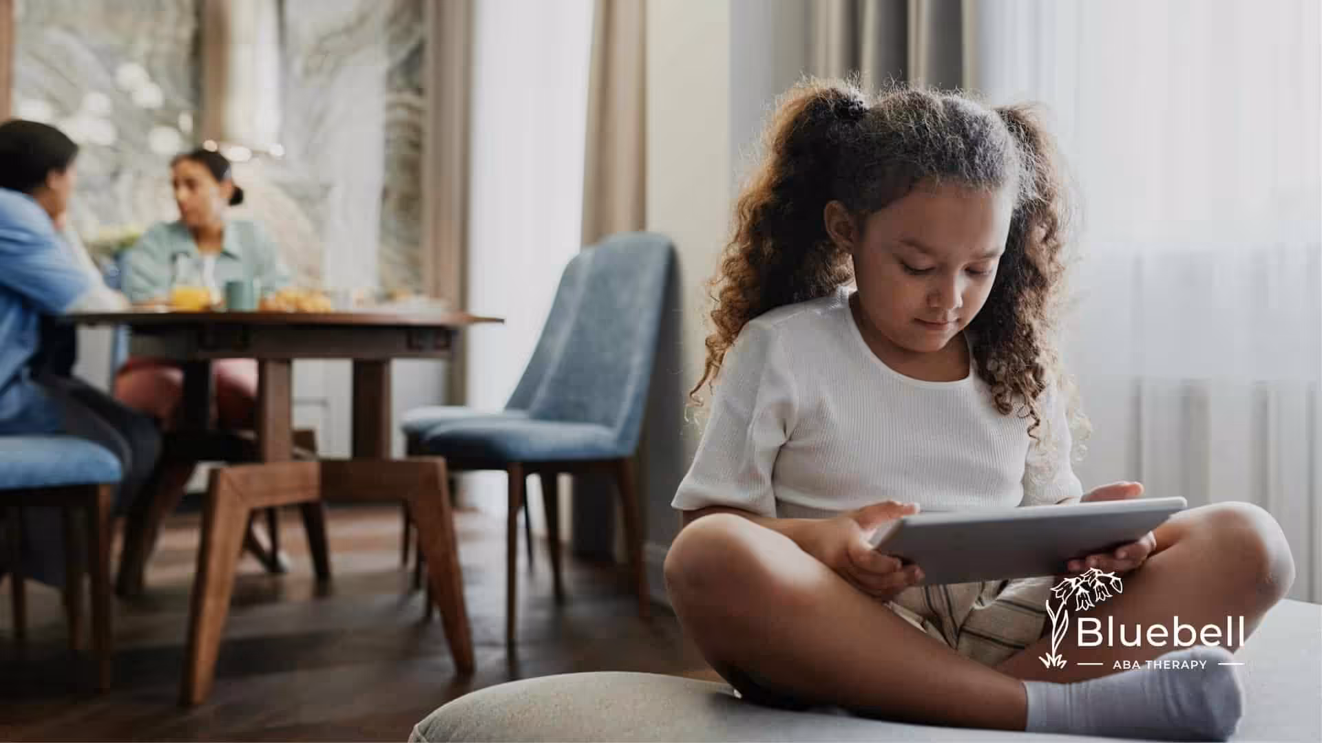An autistic girl using a tablet while her family chats at the background in North Carolina.