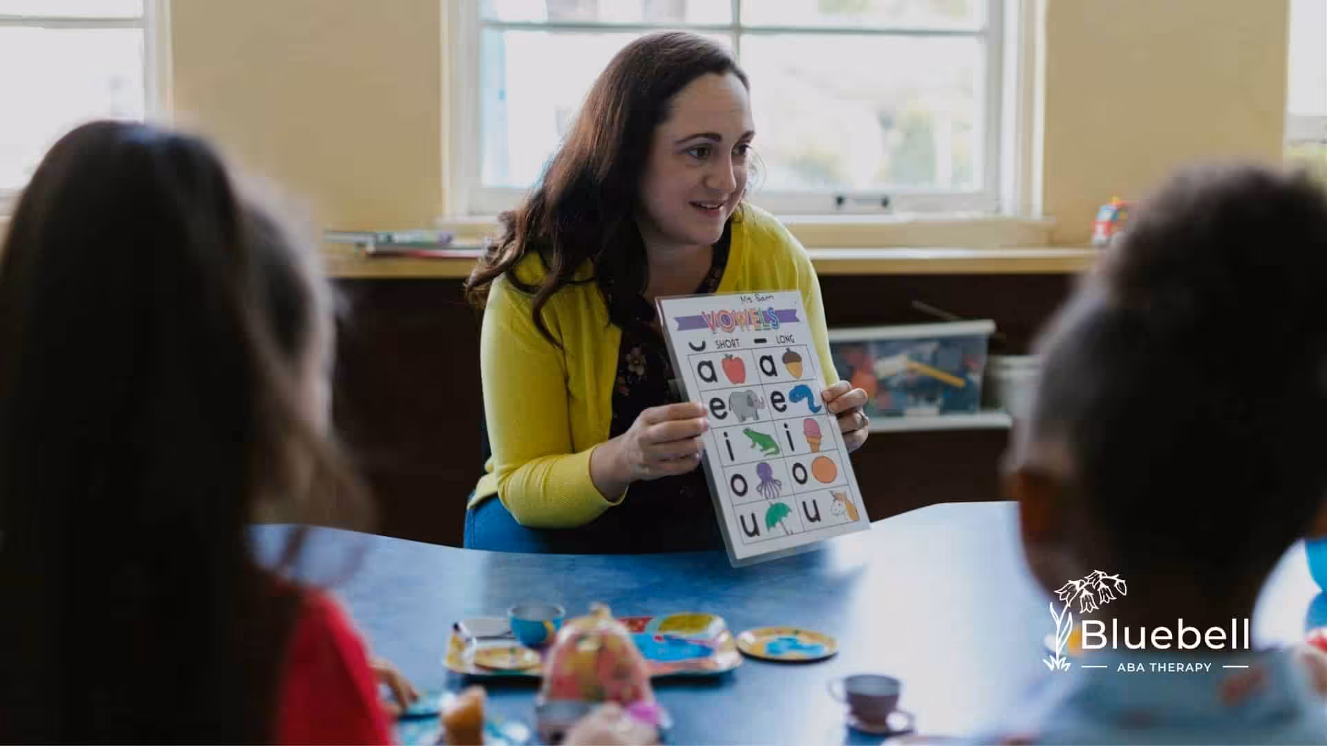 ABA therapist holding a chart with vowels, explaining it to autistic children during activity in NC.