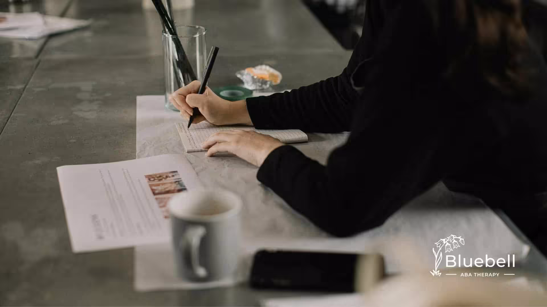 An RBT student writing in a notebook at a table while studying with a cup of coffee nearby in NC.