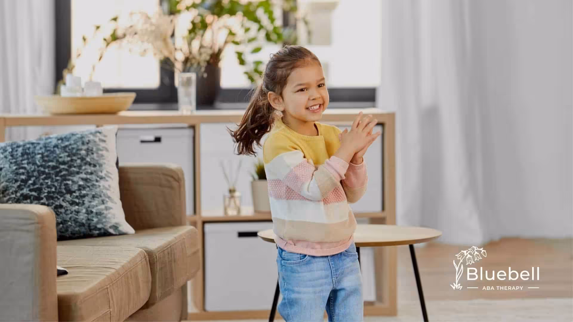 A young girl in a yellow and pink striped sweater clapping and smiling.