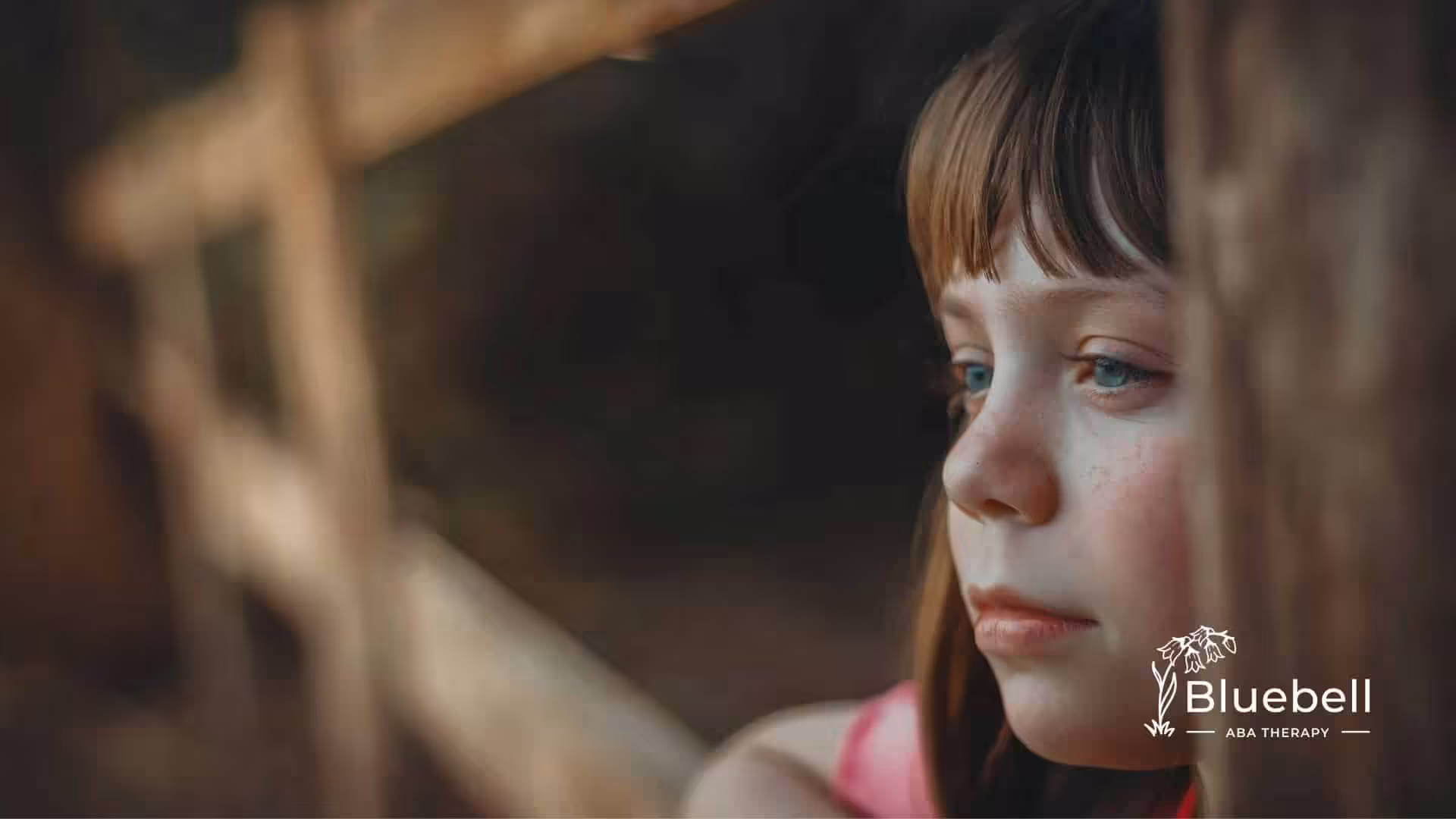 A young autistic girl gazing thoughtfully through a wooden fence at a natural outdoor setting in NC.