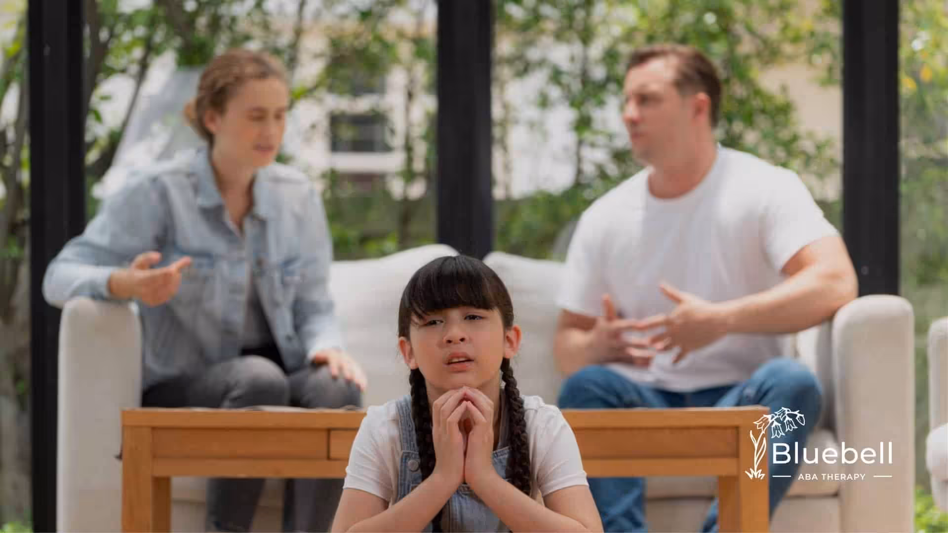 Autistic girl sitting sadly while her parents argue in the background.