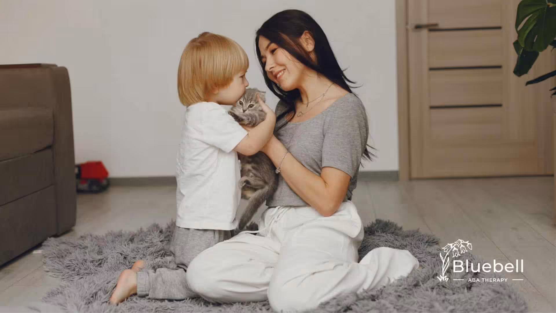 Mother and her young cuddling a small kitten in their living room.