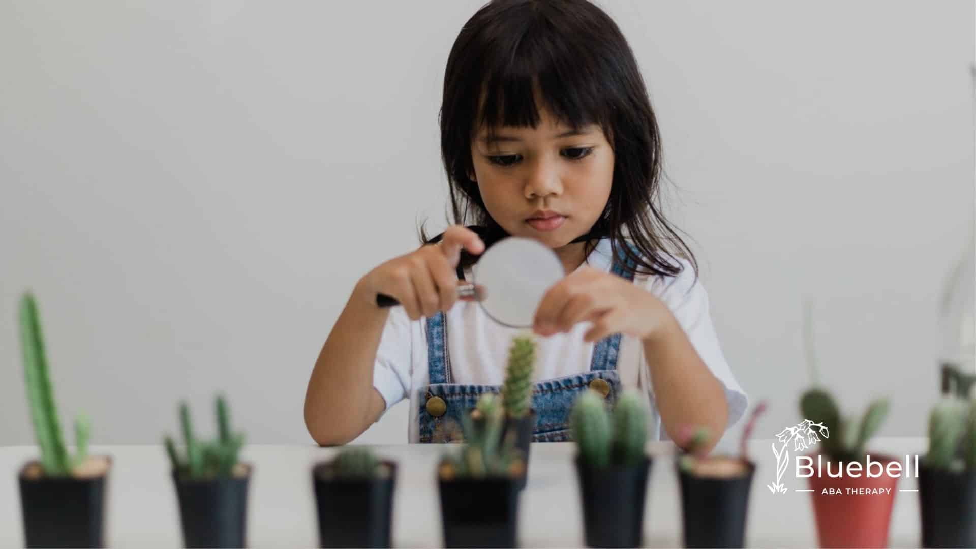 Autistic girl using a magnifying glass to closely examine small potted plants.