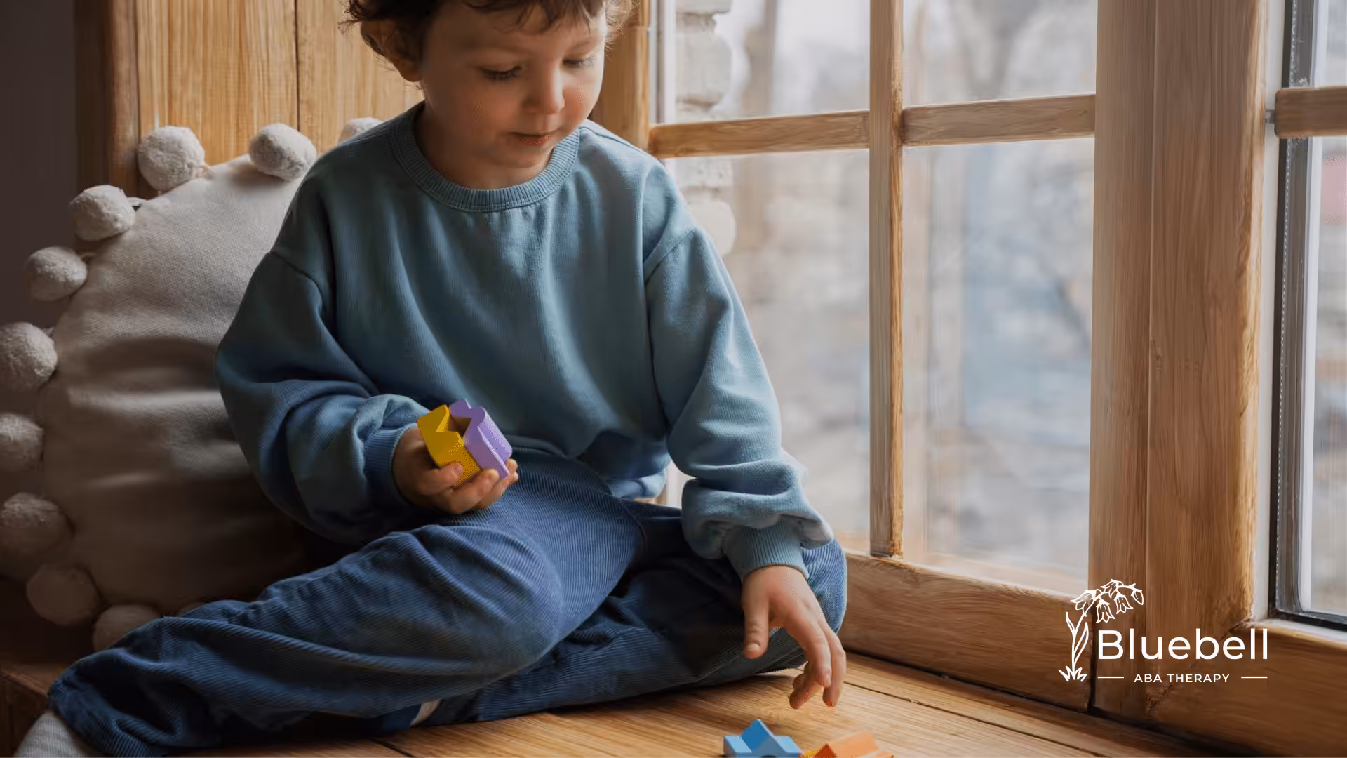 A neurodivergent child sitting in front of a window playing with colorful blocks