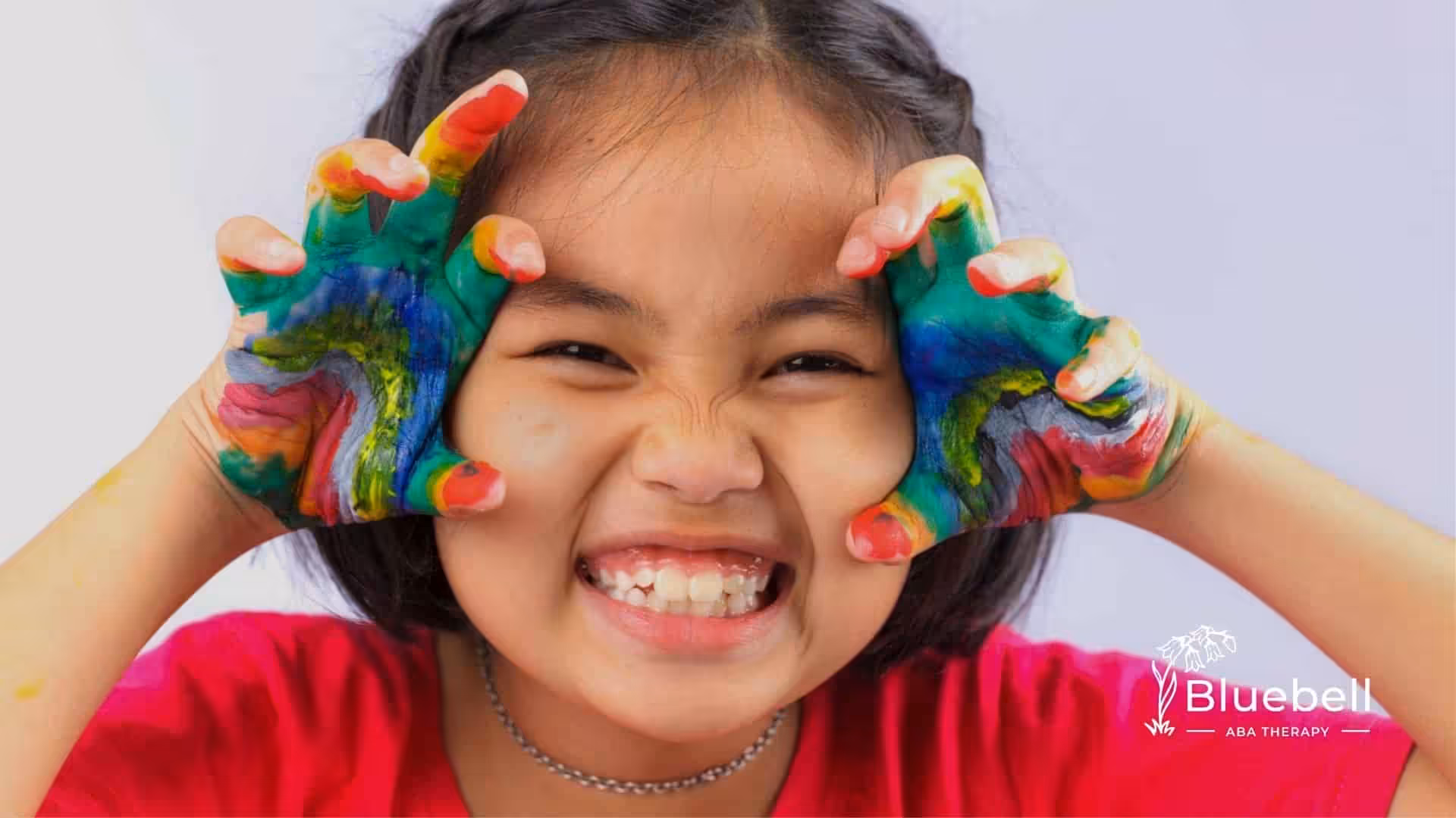 Autistic girl with colorful paint on her hands, smiling and making a playful face.
