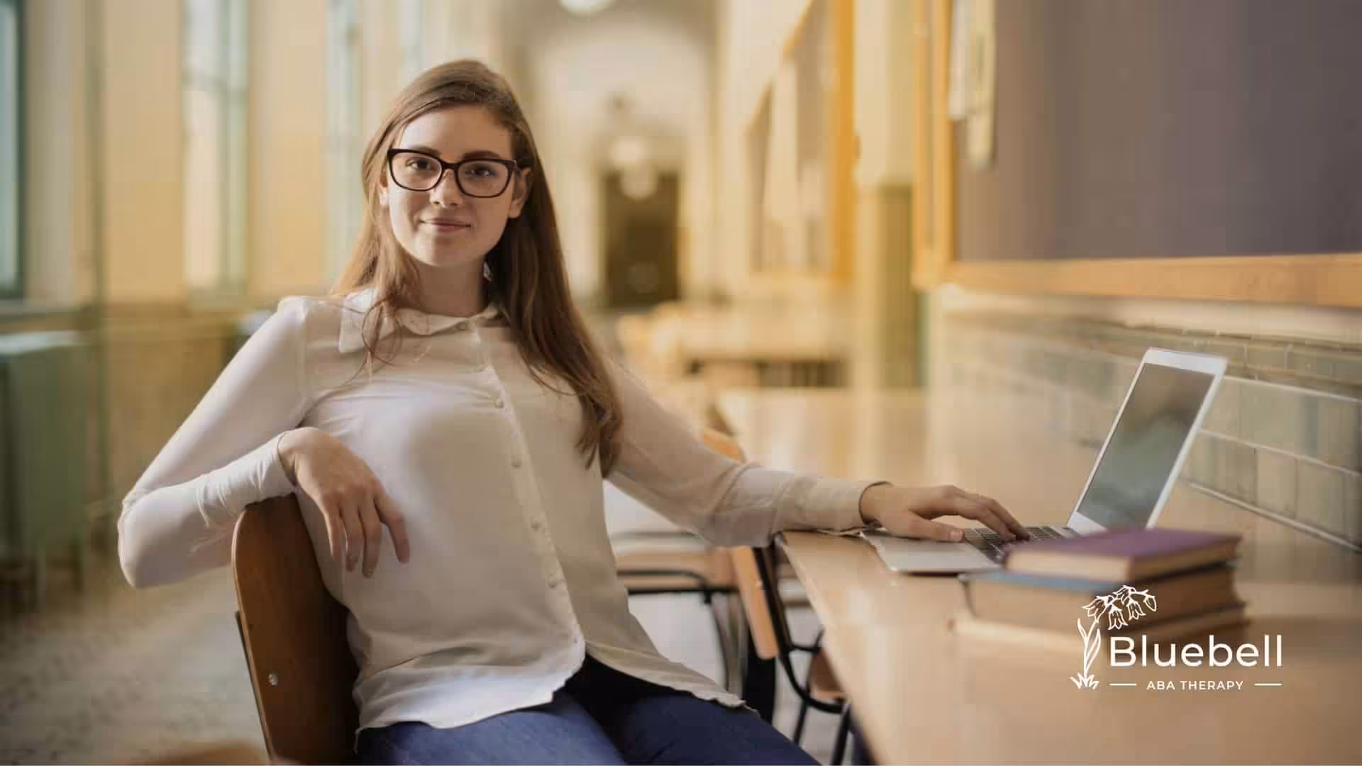 Young ABA therapist using a laptop at a school hallway with ABA therapy books on the desk in NC.