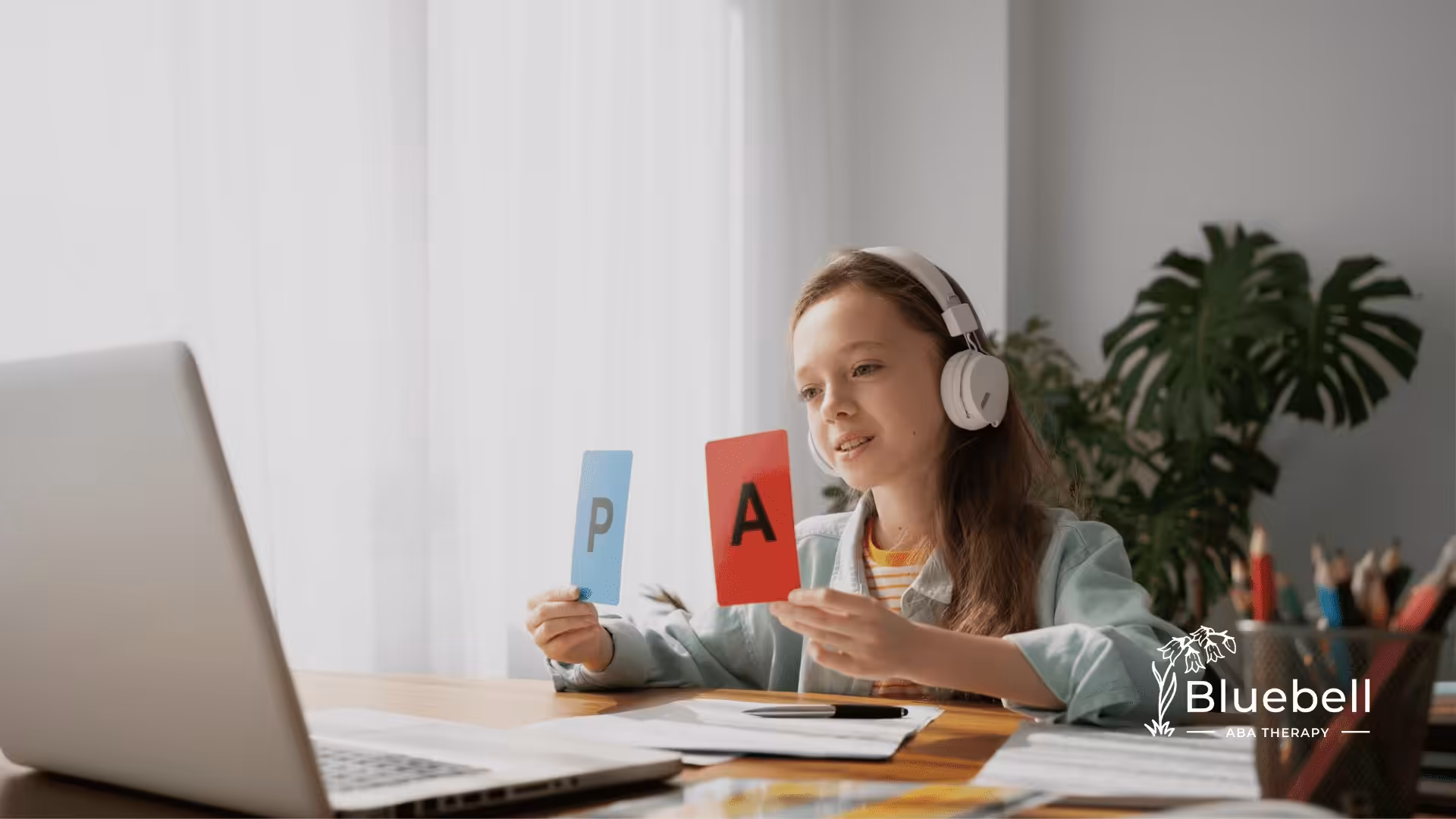 A girl is wearing headphones while holding two letter flashcards up the computer