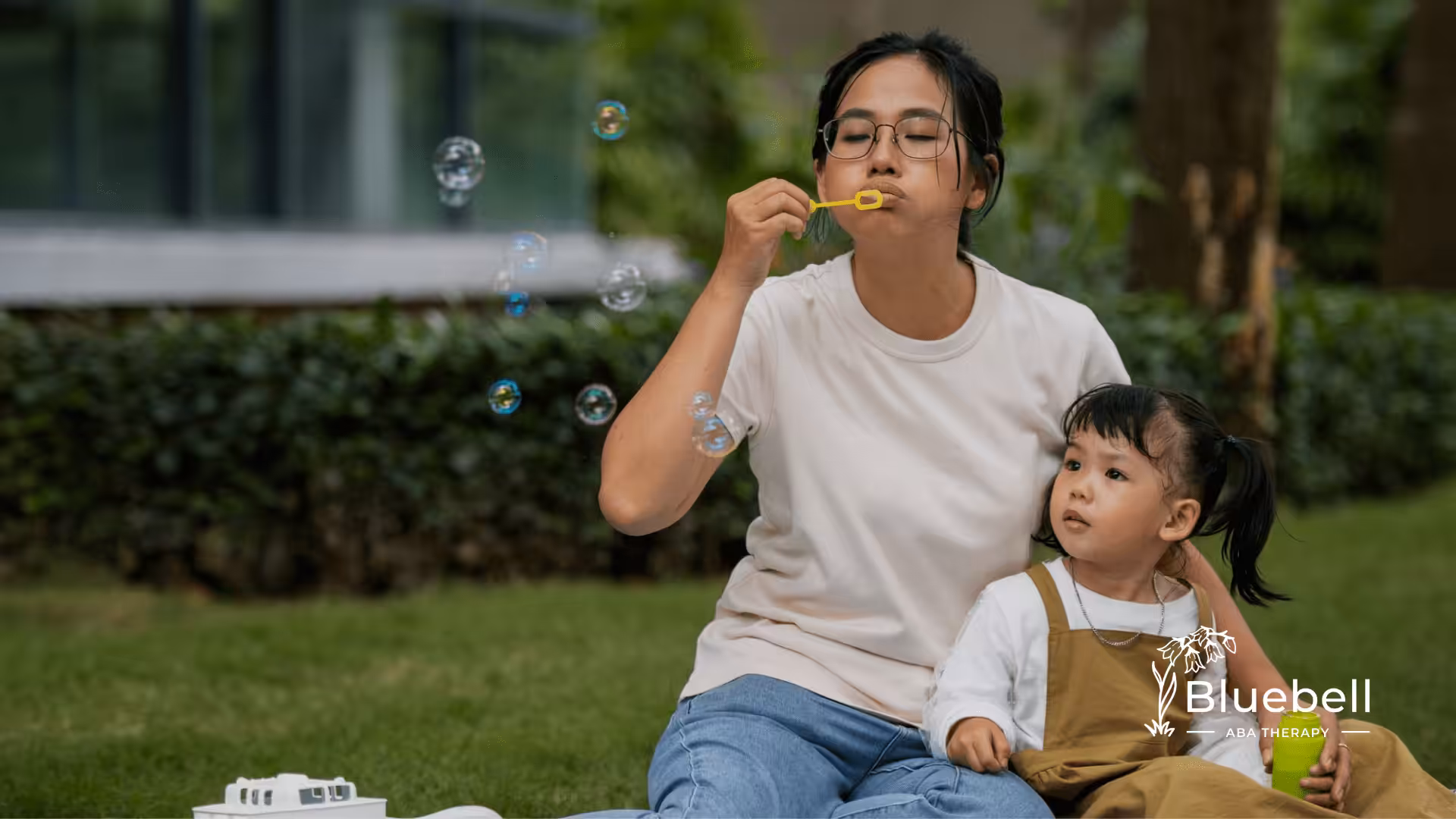 A mother and her child with autism are sitting on a park while blowing bubbles