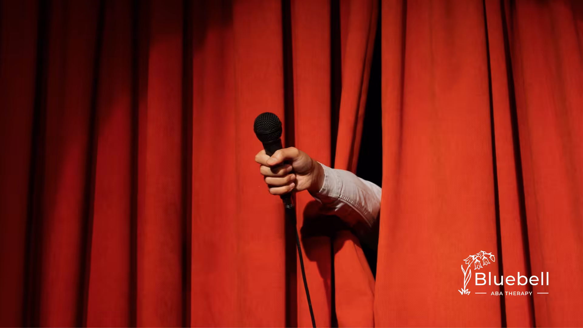 A red stage curtain with a comedian holding a microphone, symbolizing Dan Aykroyd’s comedy career.