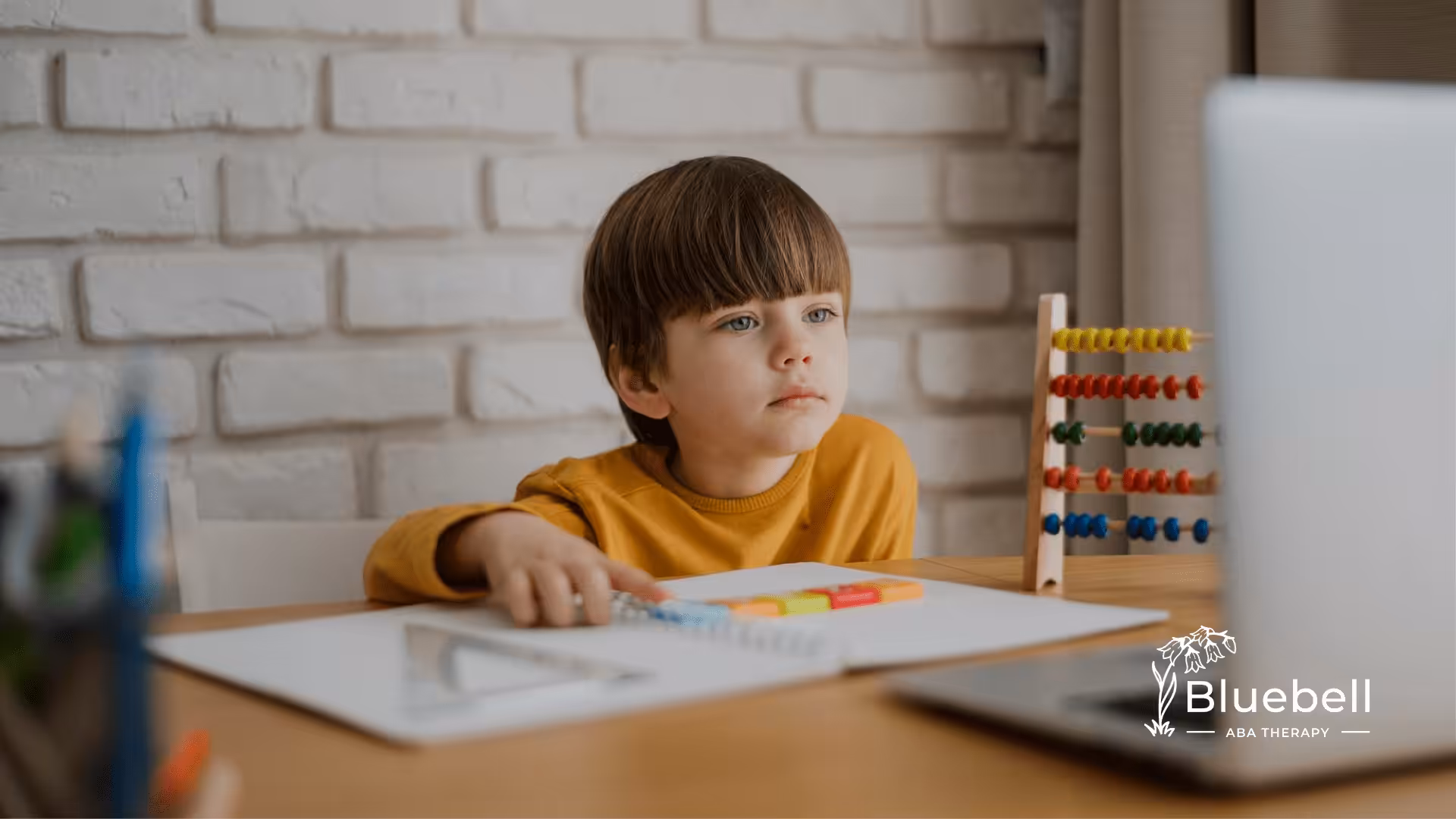 A kid with autism sitting on a table with papers and colored pens
