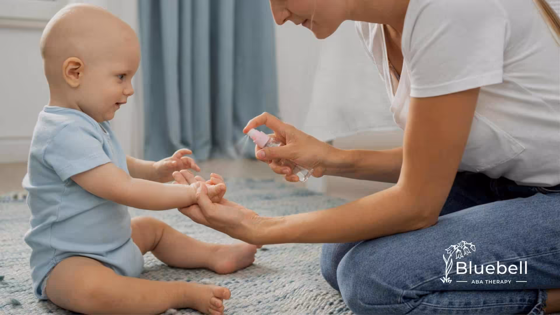 BCBA sprays baby’s hands while sitting on floor.