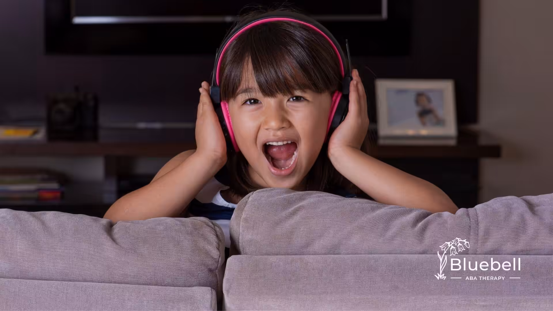 Autistic girl with pink headphones sitting on a couch.