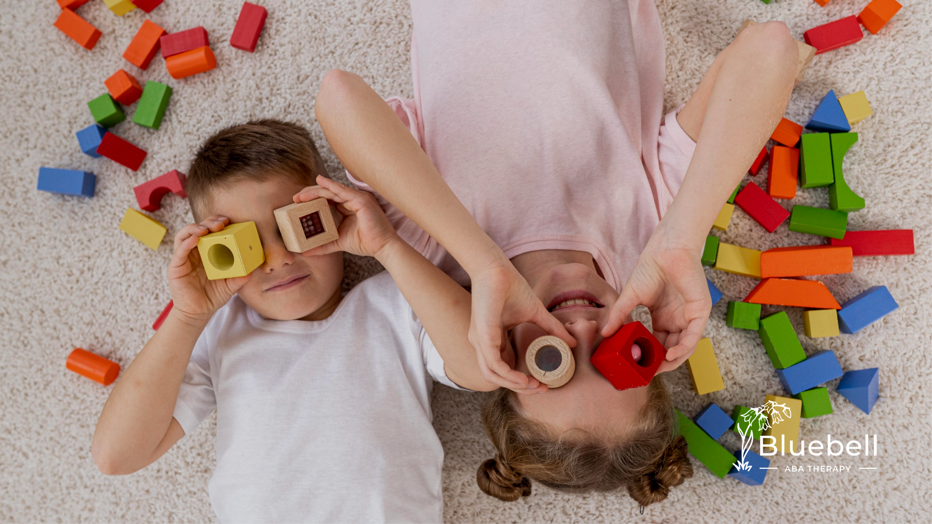 Two kids are laying on a floor mat playing with colorful toys