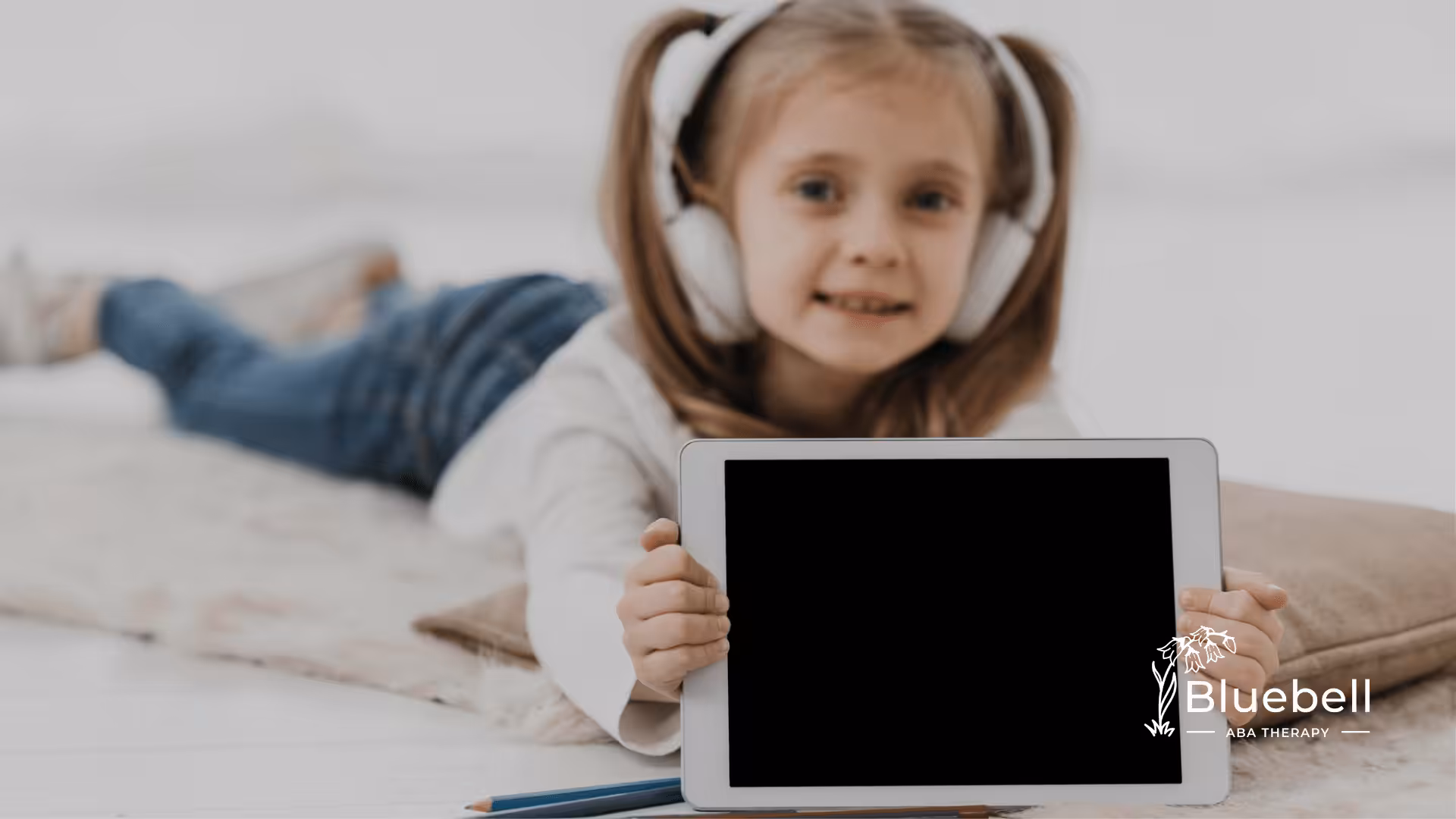 A child laying on a couch wearing a pair of headphones while holding an iPad