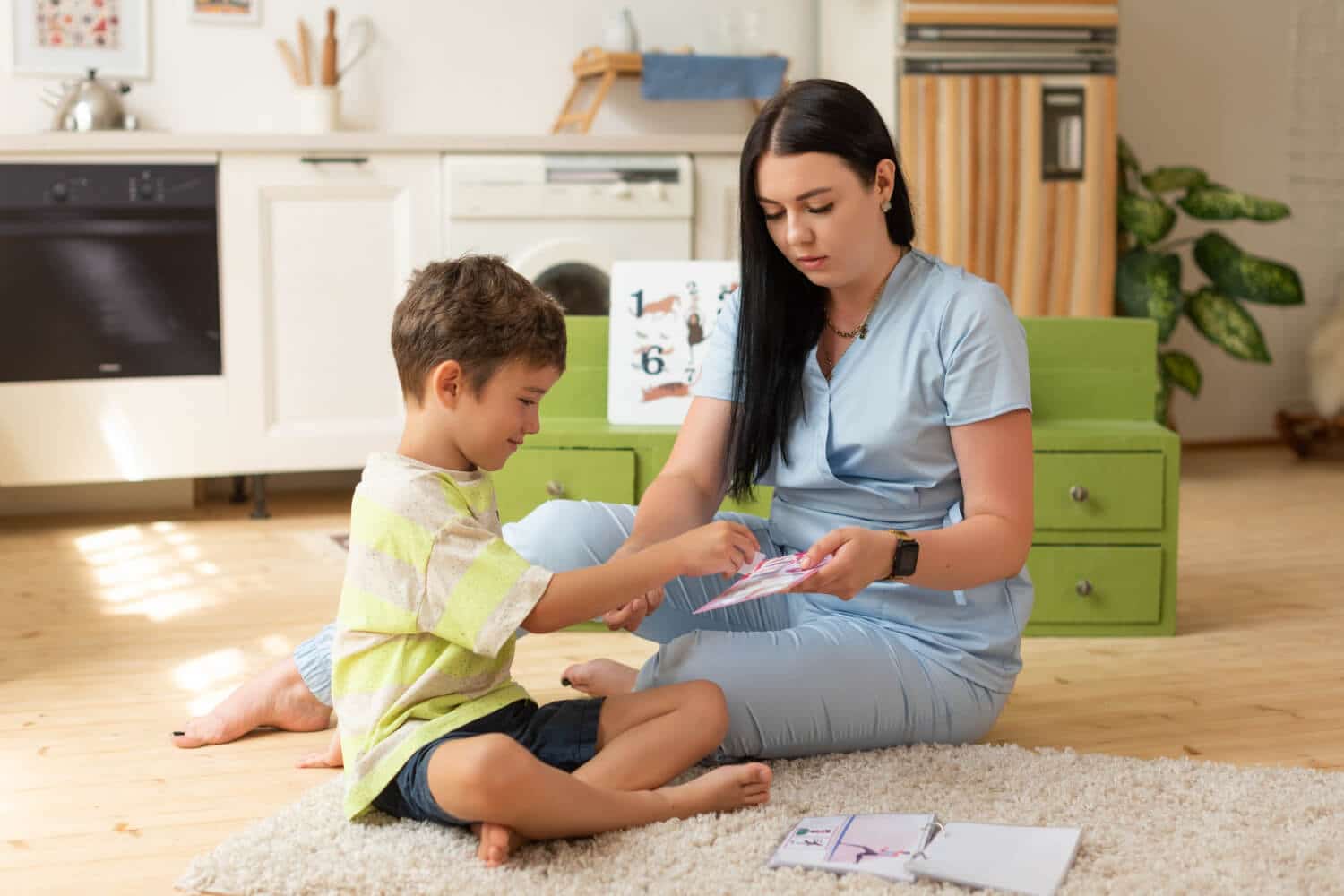 ABA therapist and young boy sit on the floor engaged in a learning activity.
