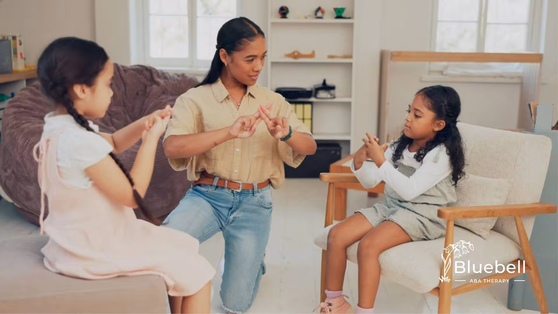An ABA therapist teaching two young girls with autism sign language in a cozy room.