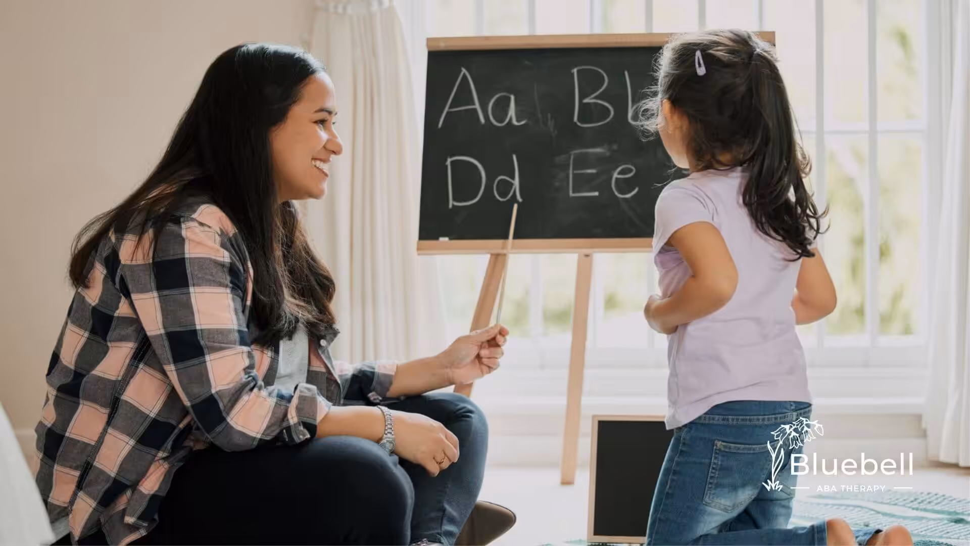 A BCBA teaching an autistic child how to write letters on a chalkboard in ABA therapy.