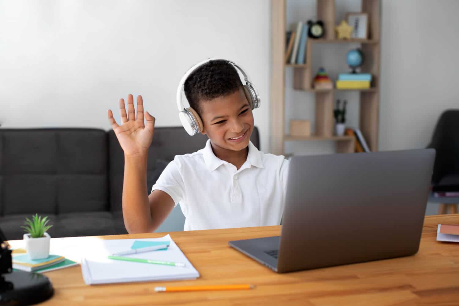 Boy wearing headphones waves at a laptop during a remote ABA session.