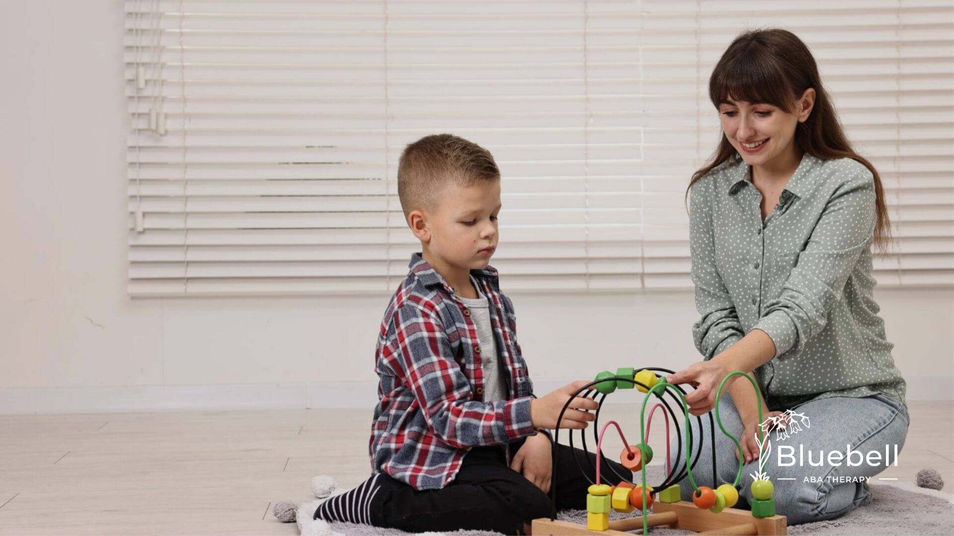 Autistic boy and ABA therapist playing with a bead maze toy on the floor in ABA therapy.