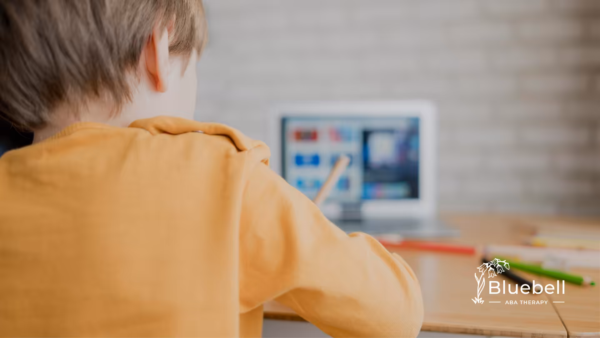 A child with autism is writing on a paper while in front of a computer