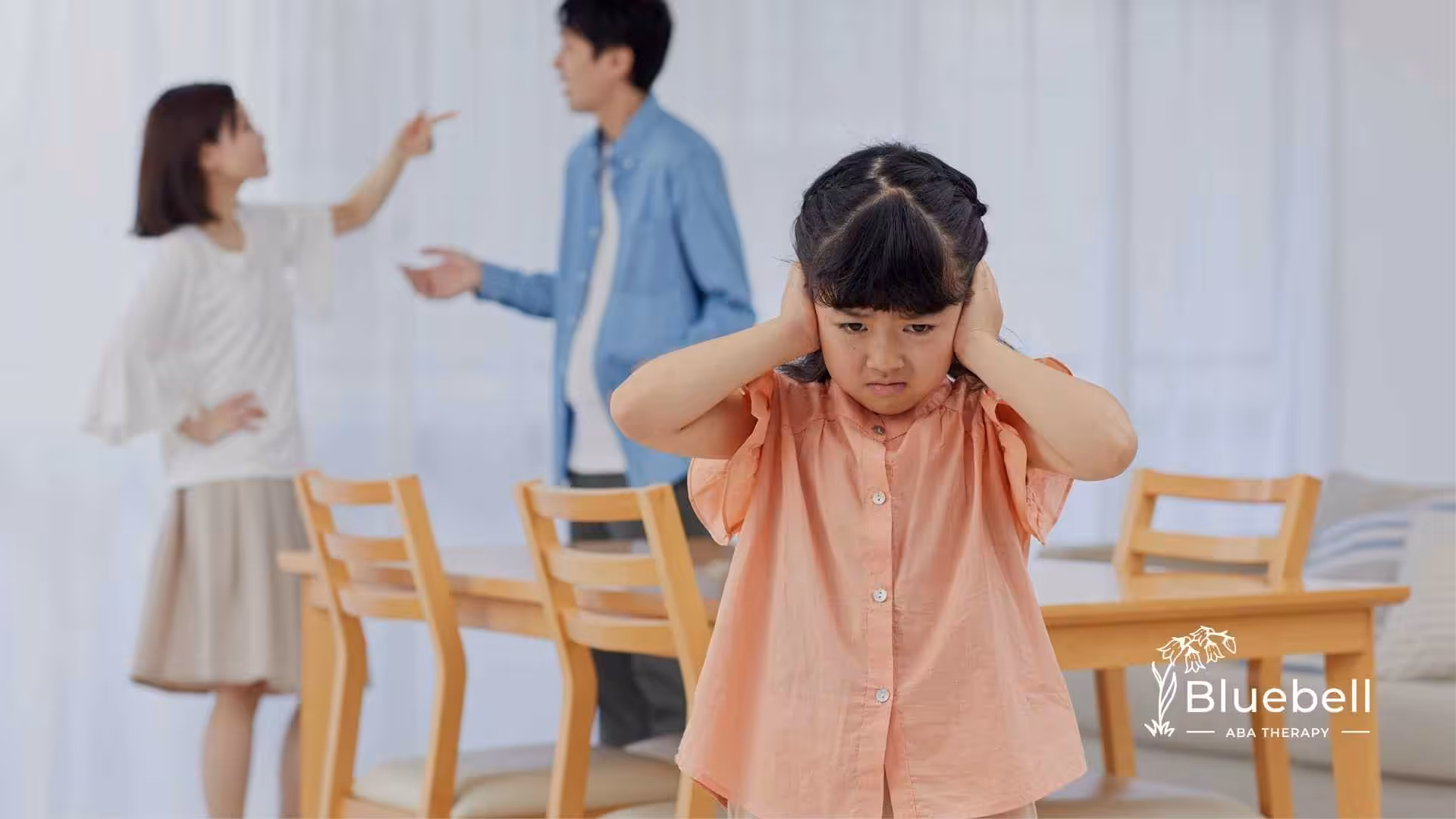 A young girl in a pink shirt covers her ears, looking distressed, while a couple in the background appears to be arguing by a dining table.