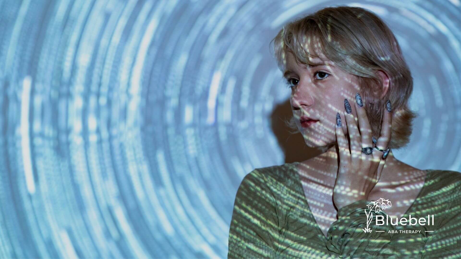 An autistic woman with abstract light patterns projected on her face and hands.