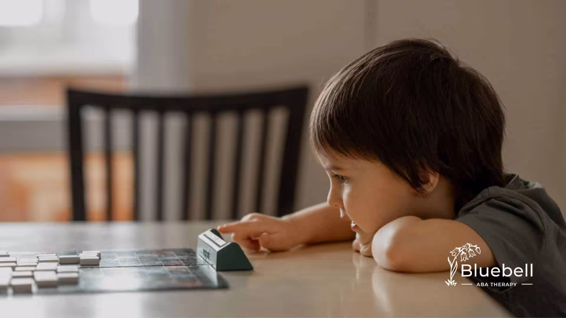 A young boy with autism focused on playing a board game on a table.