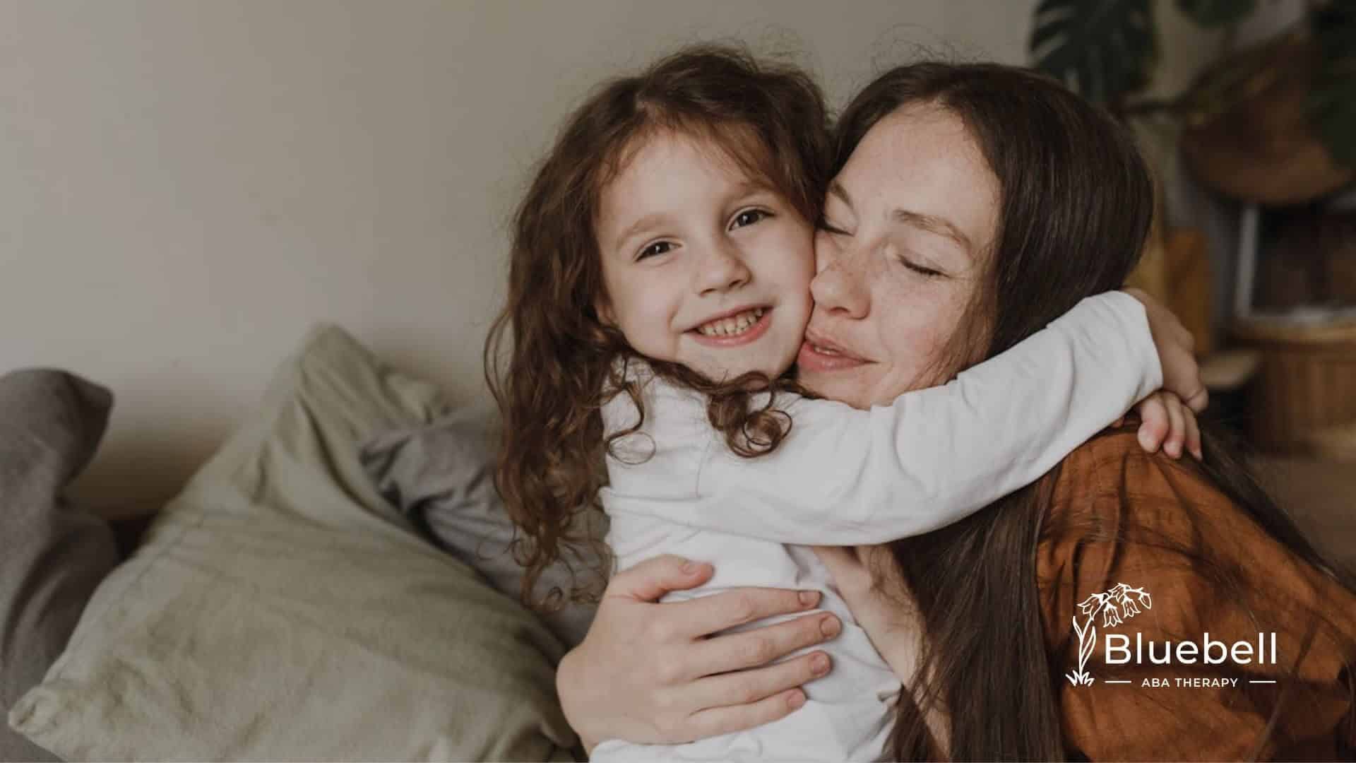 A young girl with autism hugs her smiling ABA therapist warmly.