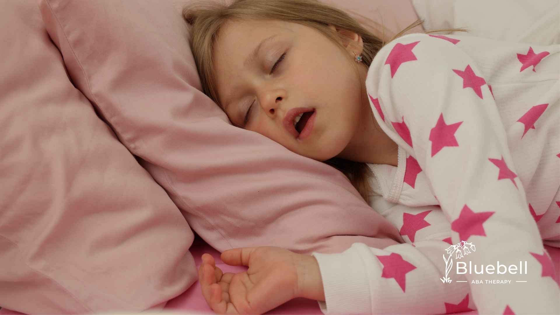 A young girl peacefully sleeps on a pink pillow with her mouth slightly open, wearing white pajamas with pink stars. The mood is calm and serene.
