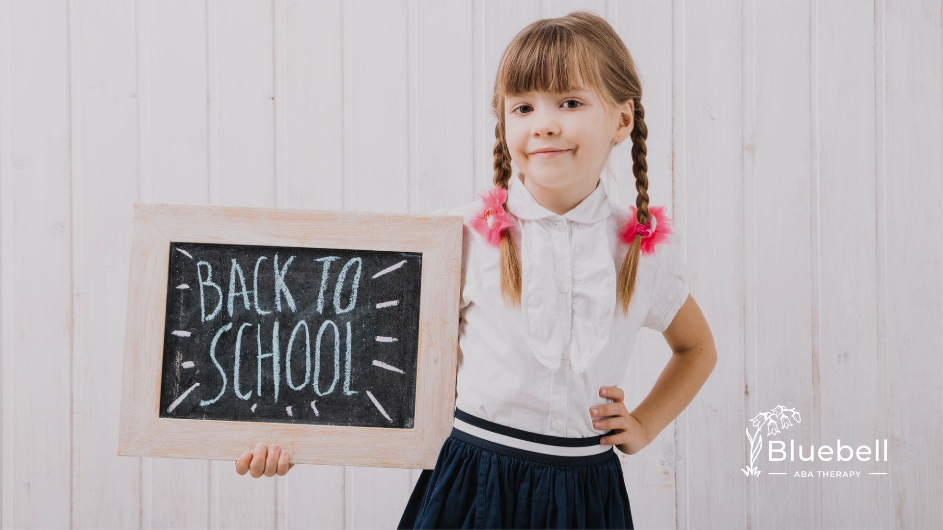 A kid with autism wearing a school uniform, holding a chalkboard with the words "back to school" written on it