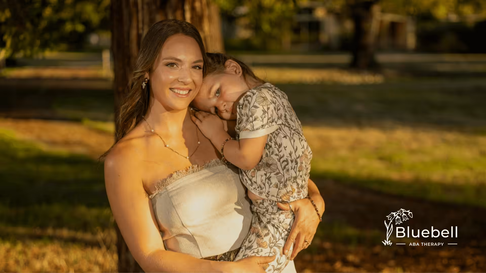 ABA therapist embraces the autistic child in sunny outdoor setting, showing warmth, closeness, and gentle affection.