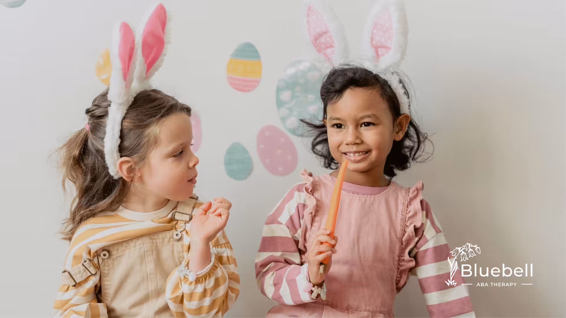 Two autistic children in bunny ear headbands sit with carrots, surrounded by pastel Easter-themed decor.
