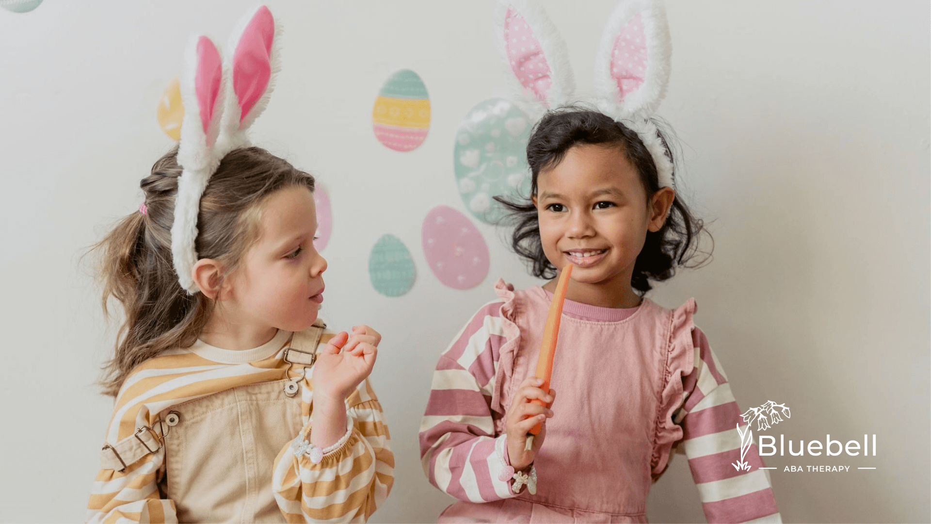 Two autistic children in bunny ear headbands sit with carrots, surrounded by pastel Easter-themed decor.