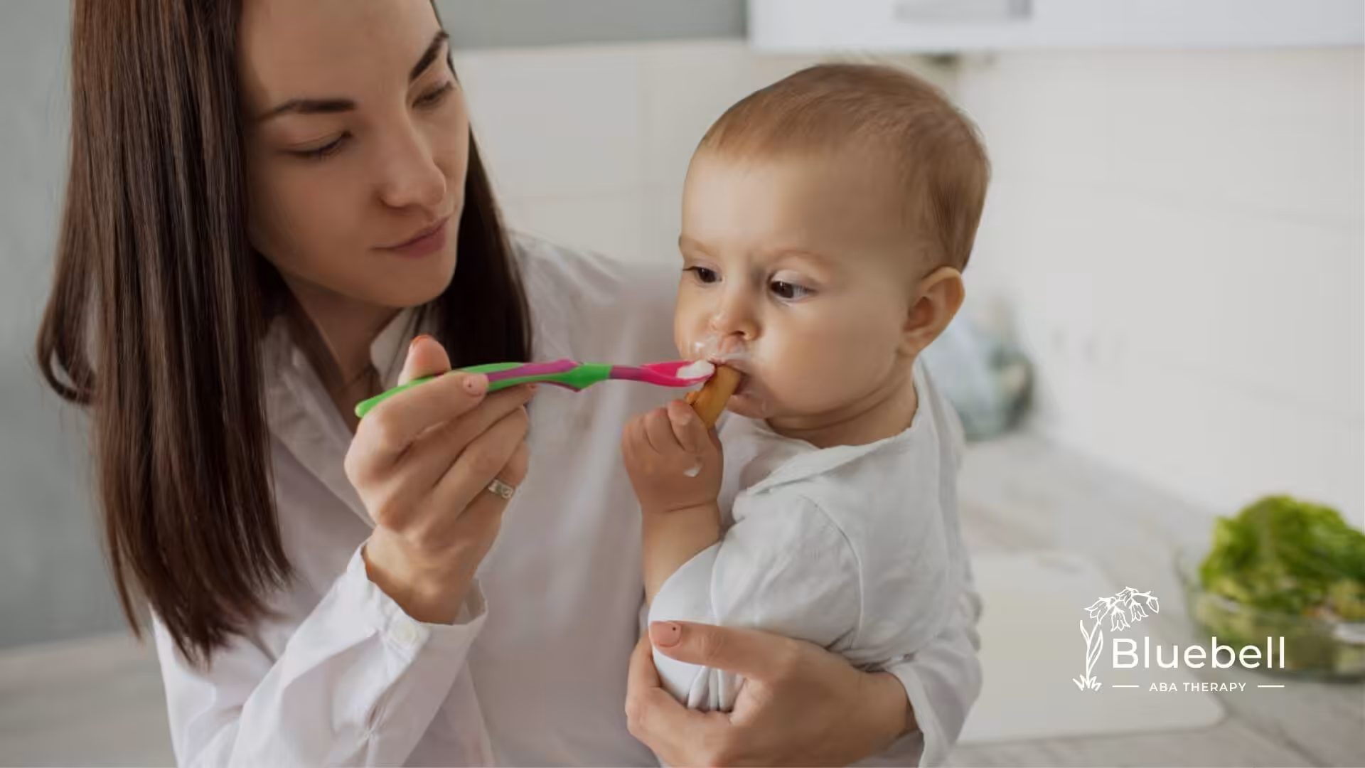 A BCBA feeds a baby with autism with a spoon while holding them in her arms.