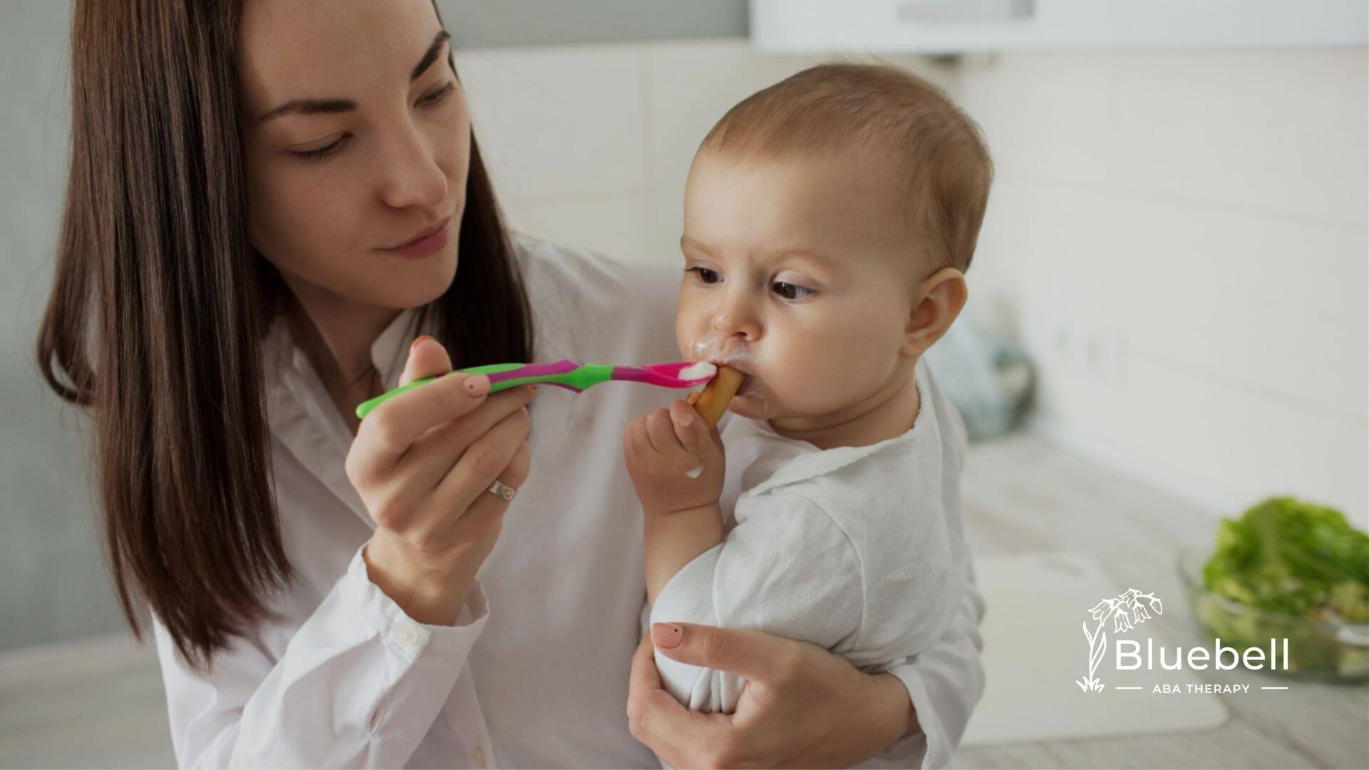 A BCBA feeds a baby with autism with a spoon while holding them in her arms.
