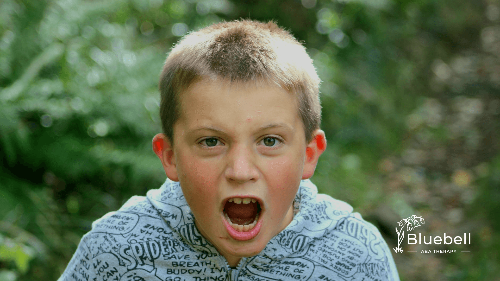 Autistic boy shouting with a serious expression with full of madness in a green outdoor setting after ABA therapy.