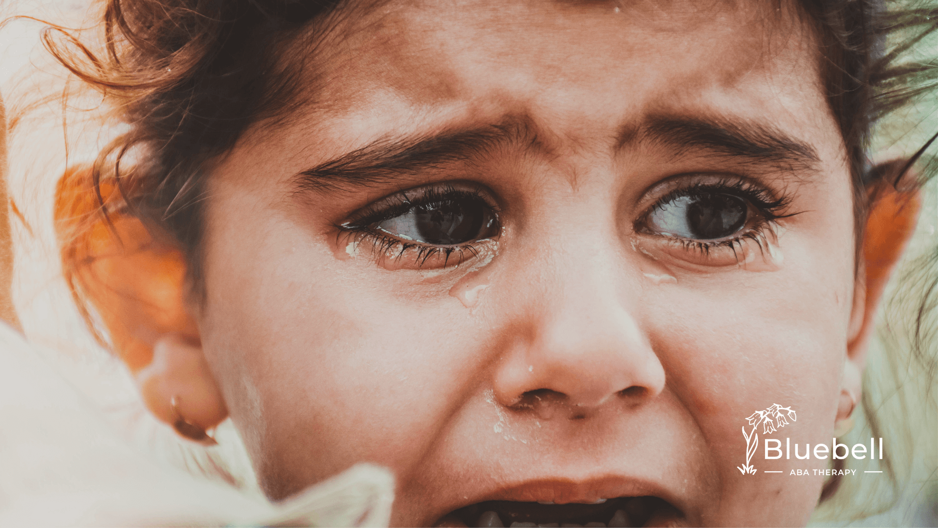 Close-up of a tearful child with wide eyes and furrowed brows, showing visible distress and emotional vulnerability.