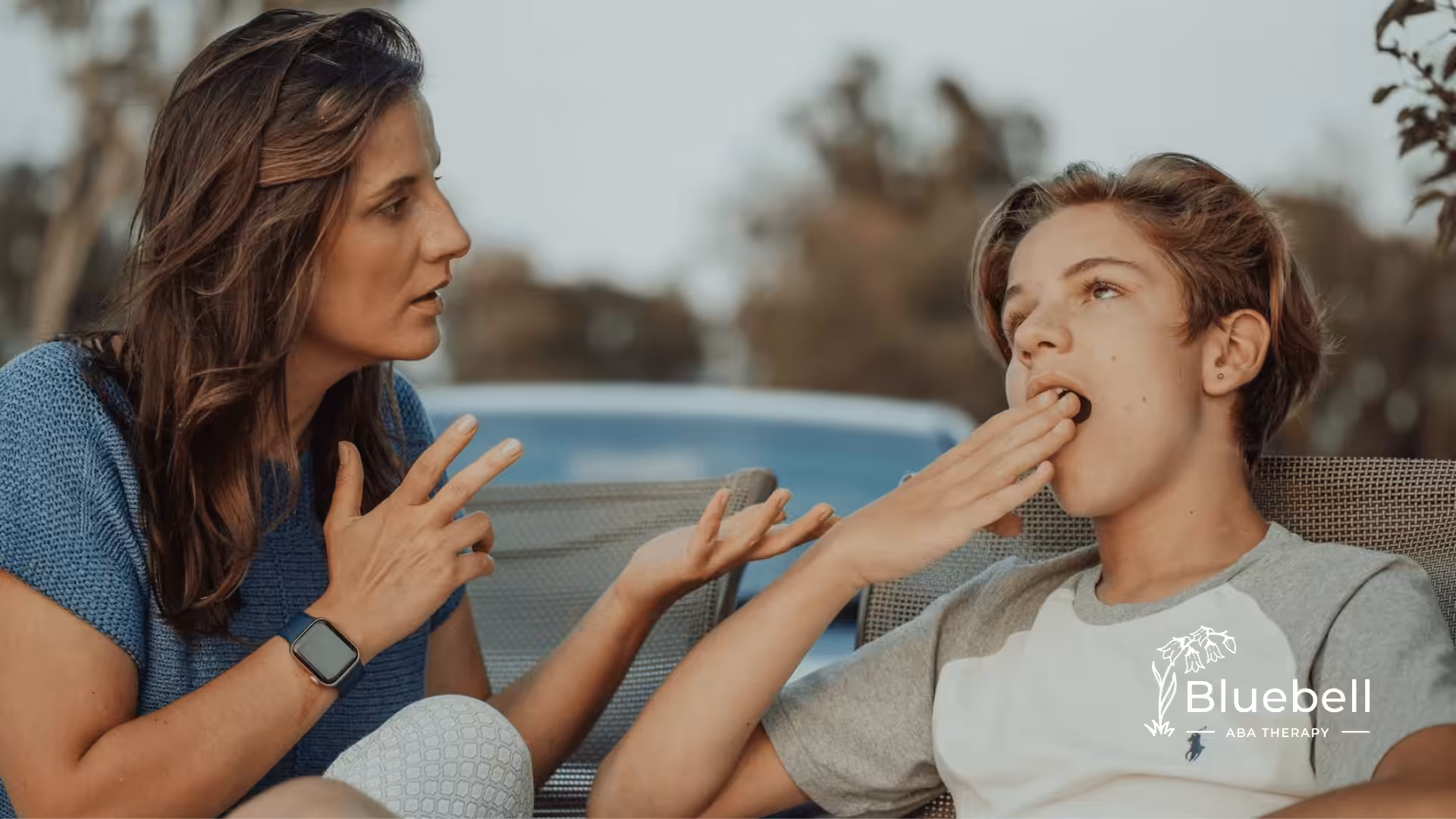 Two people converse outside; one uses hand gestures while the other yawns, appearing tired or bored.
