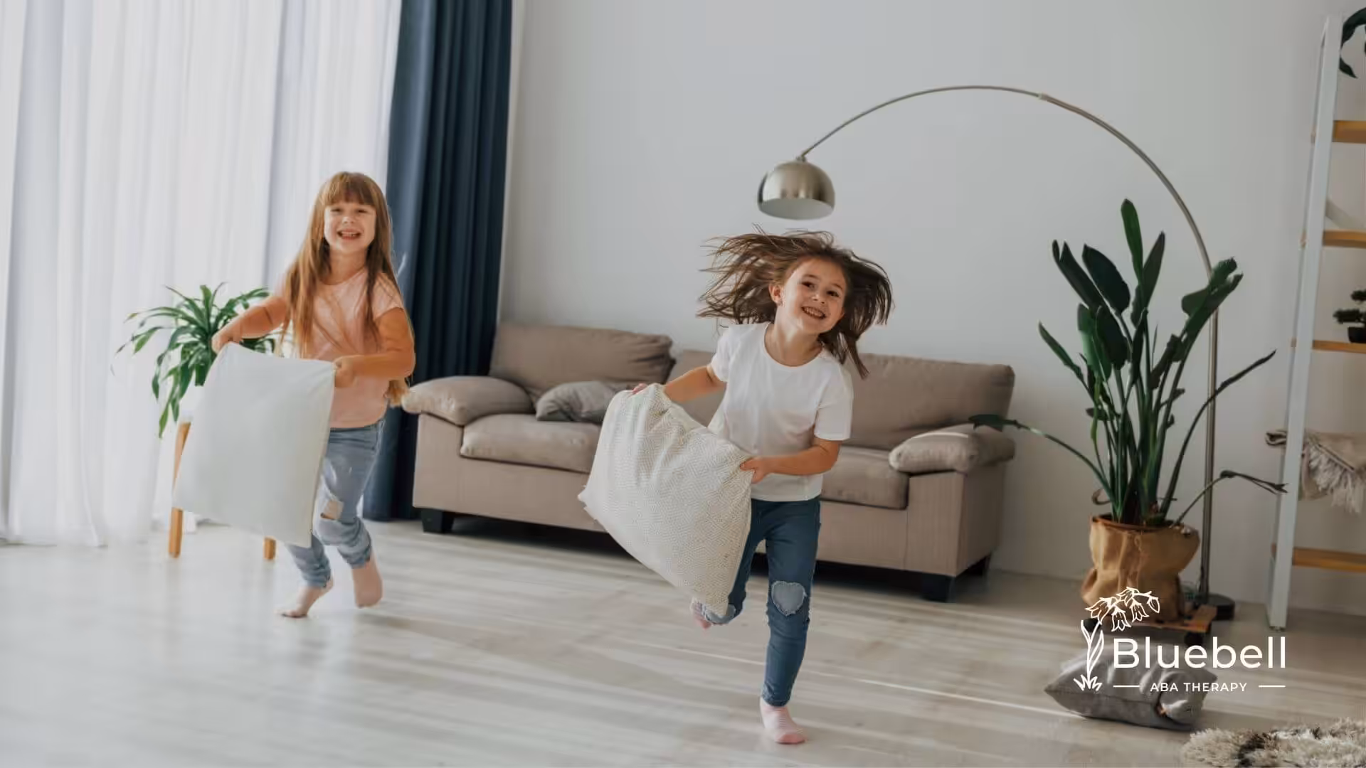 Two young girls with autism running and playing with pillows in a modern living room.