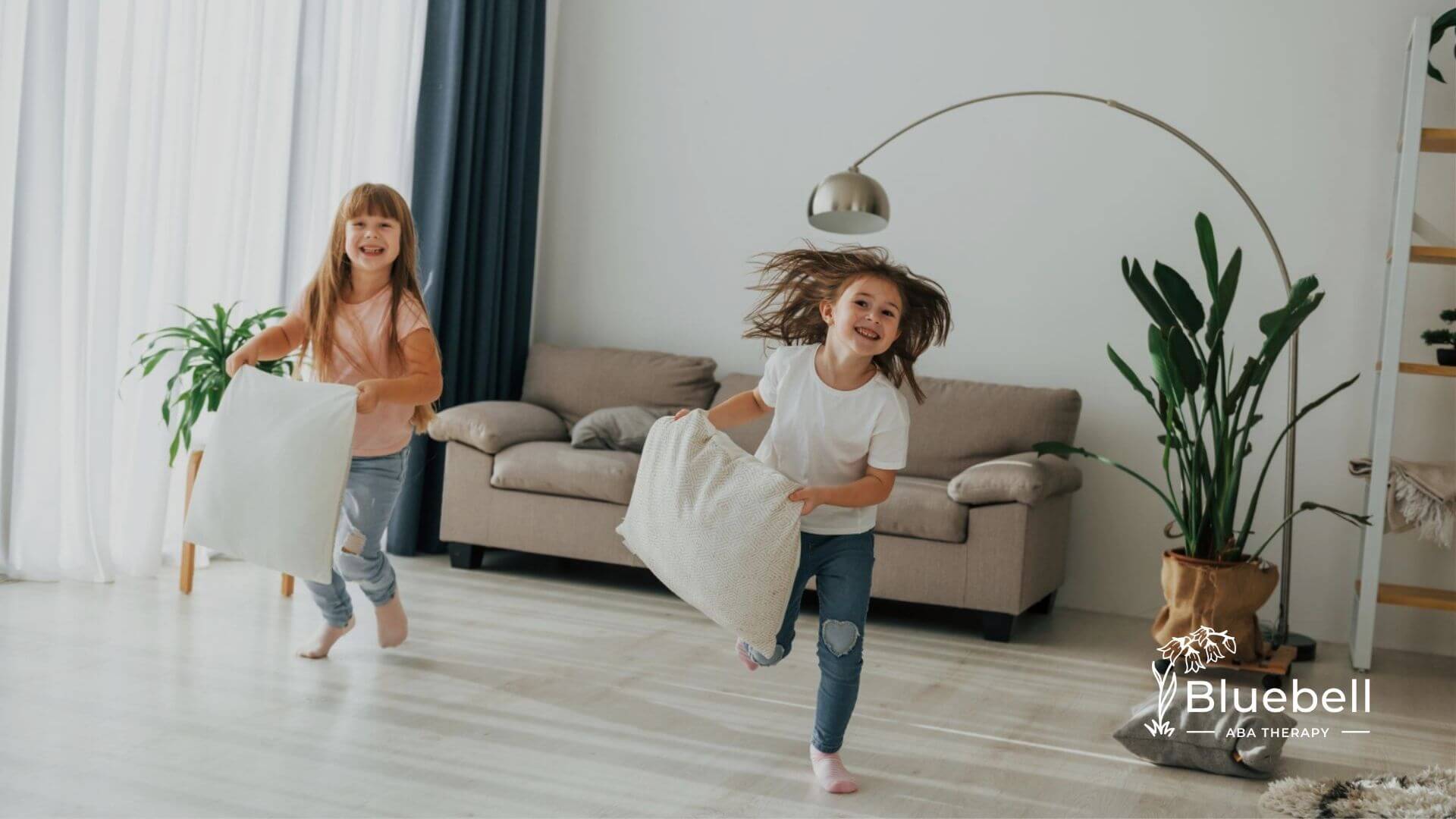 Two young girls with autism running and playing with pillows in a modern living room.
