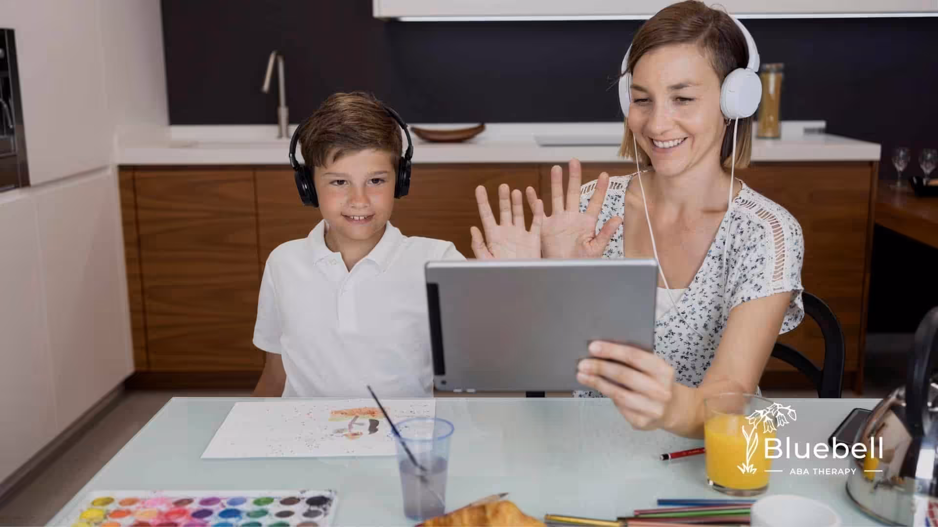 A therapist and an autistic kid wearing headphones and waving during a virtual therapy session, representing online therapy.