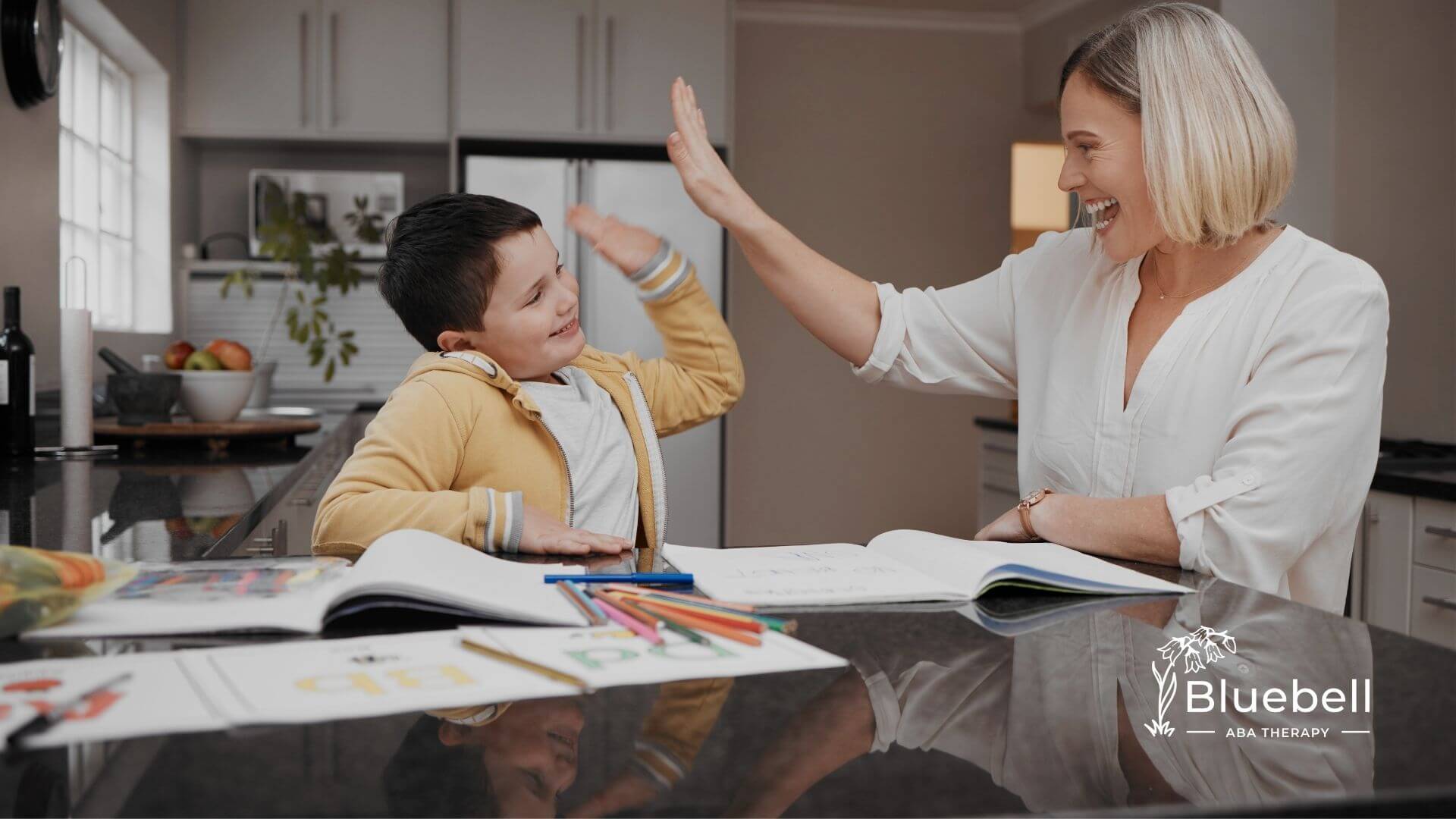 Female therapist giving a high five to autistic girl at a table, reinforcing positive behavior and learning success at home.