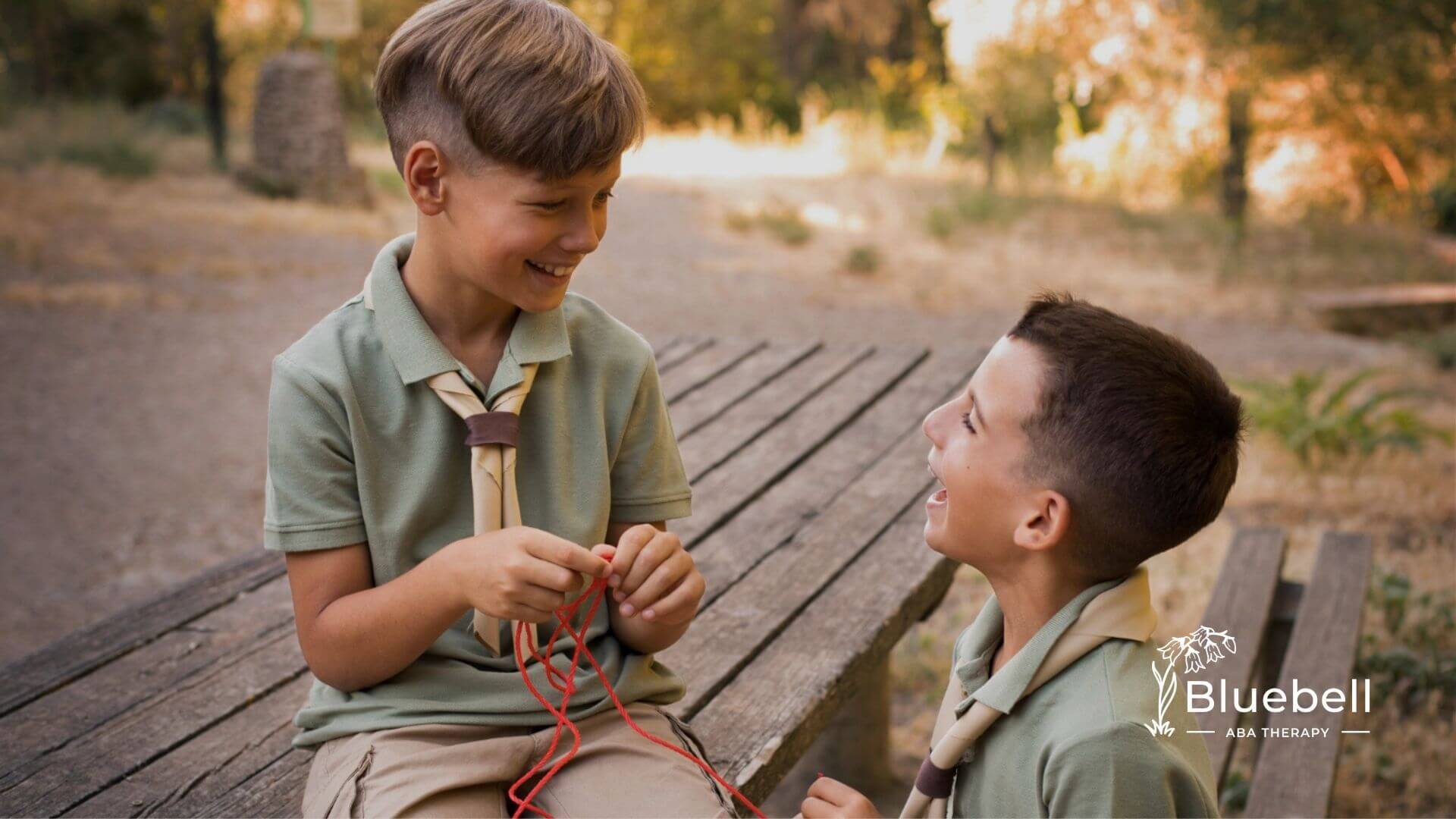Two boys with autism smiling and playing together outdoors, one holding a red rope.