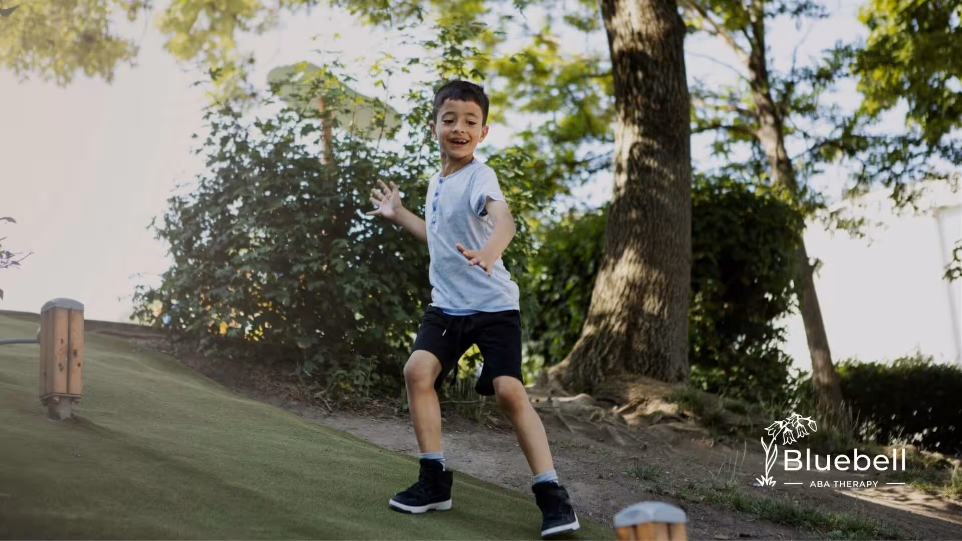 An autistic boy balancing on a grassy hill in a park, practicing coordination and motor planning during outdoor play time.